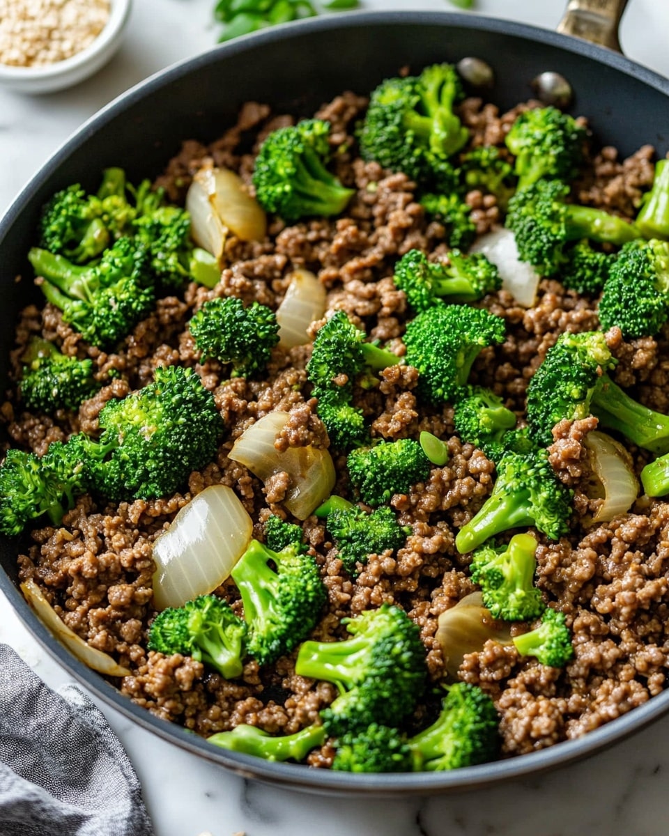 Ground Beef and Broccoli Stir Fry, easy beef broccoli stir fry, healthy beef stir fry, quick ground beef recipes, savory beef broccoli dish A white bowl filled with three main layers: the bottom layer is light brown cooked rice with a slightly oily texture, the middle layer has bright green broccoli florets and strips of red bell pepper scattered across, and the top layer consists of dark brown cooked ground meat topped with a glossy sauce. Small white sesame seeds are sprinkled over the meat, and finely chopped green onions are scattered on top and around the bowl edges. The bowl sits on a white marbled surface with a white cloth napkin nearby, and a small white bowl of white sesame seeds is in the upper right background.