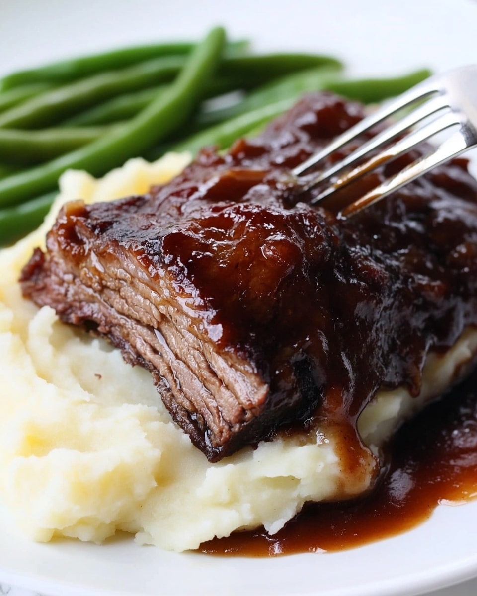 A white plate holds a thick piece of dark, glazed meat resting on a bed of creamy, light-colored mashed potatoes with a smooth texture. To the side, there is a small pile of bright green beans, adding a fresh pop of color. The plate sits on a white marbled surface with a slightly blurred background showing part of a silver kitchen appliance. The lighting highlights the glossy texture of the meat and the softness of the potatoes. Photo taken with an iphone --ar 4:5 --v 6.1