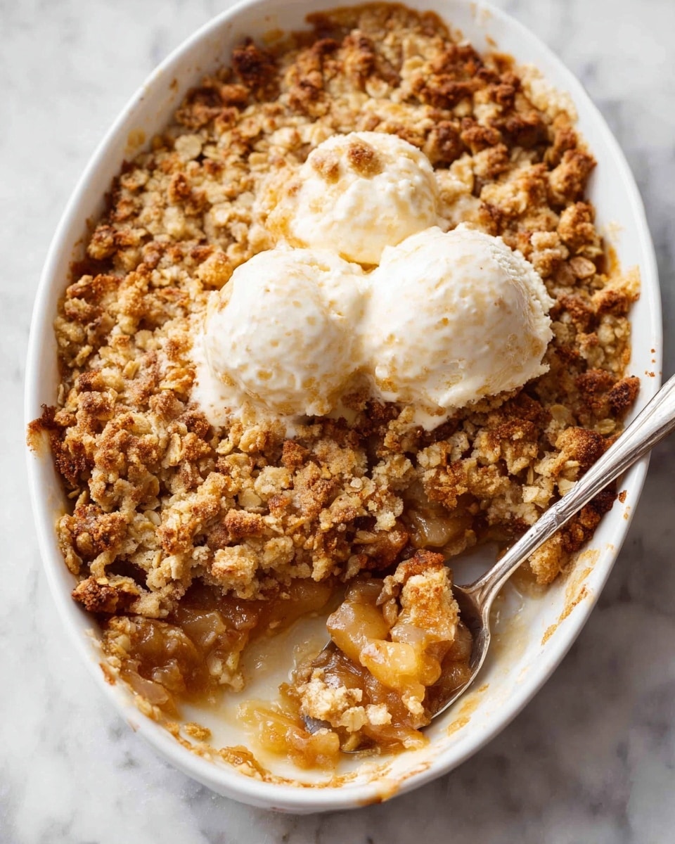 The image shows a white oval dish filled with a baked crumble dessert. The top layer is crumbly and golden brown with chunks of oats and nuts, giving it a rough texture. In the middle of the dish, there are two small scoops of melting white ice cream, partially covering the crumble. A spoonful has been taken from the bottom right, revealing a soft, gooey layer of cooked fruit beneath the crunchy top, in light brown and golden colors. The dish is set on a white marbled surface. Photo taken with an iphone --ar 4:5 --v 7