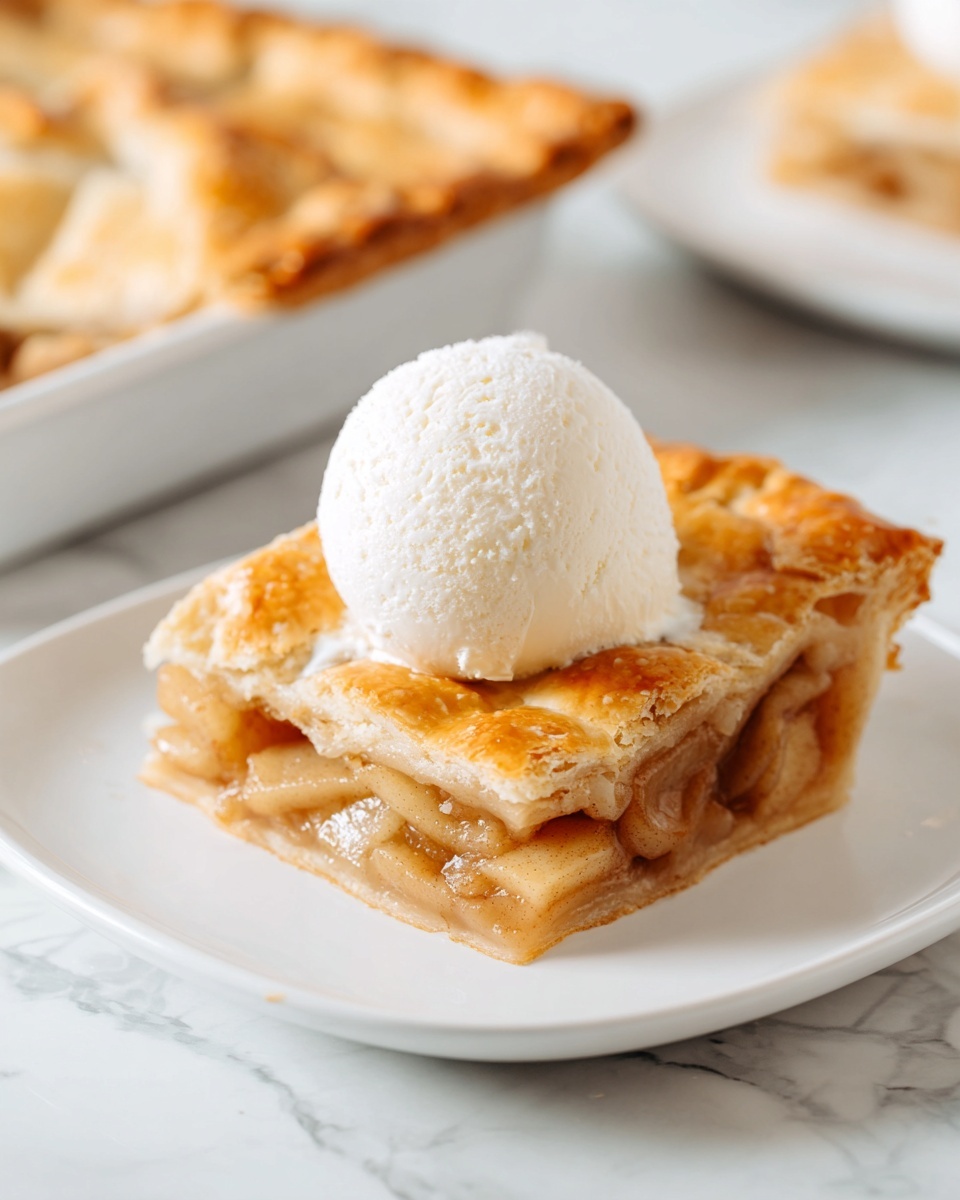 Apple Slab Pie - Cozy, Easy, and Perfect for Fall 1 A white square plate holds a single square piece of golden brown apple pie with a flaky crust showing soft cooked apple filling inside. On top of the pie slice sits a round scoop of smooth white vanilla ice cream. The plate is placed on a white marbled surface. Photo taken with an iphone --ar 4:5 --v 7