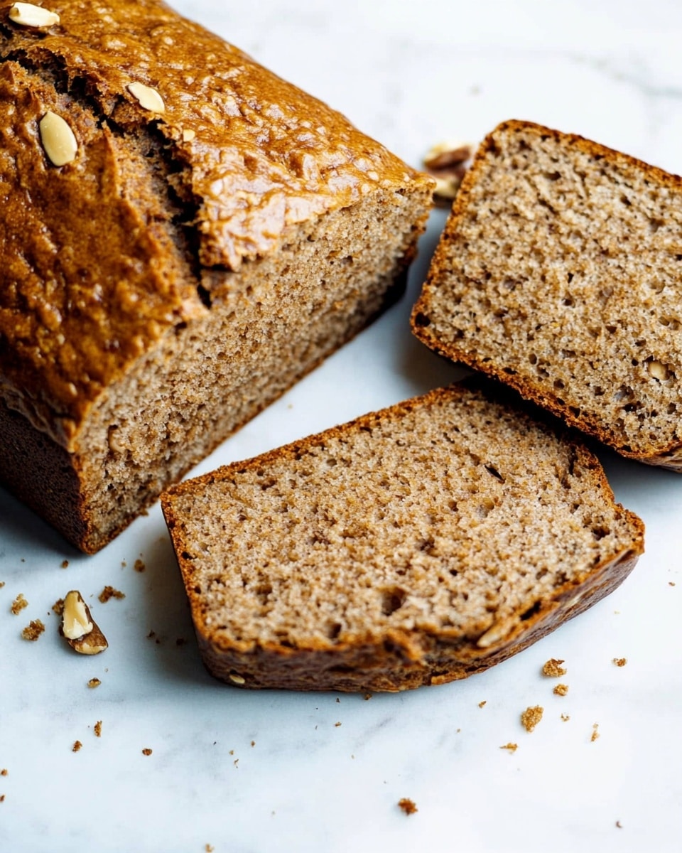 The image shows a loaf of brown bread with a shiny, golden-brown crust and a visible crack on top. The loaf is placed on a white marbled surface and is partially sliced, revealing three pieces with a soft, textured inside filled with small dark bits and nuts. A blue cloth is partially visible in the background. Photo taken with an iphone --ar 4:5 --v 6.1