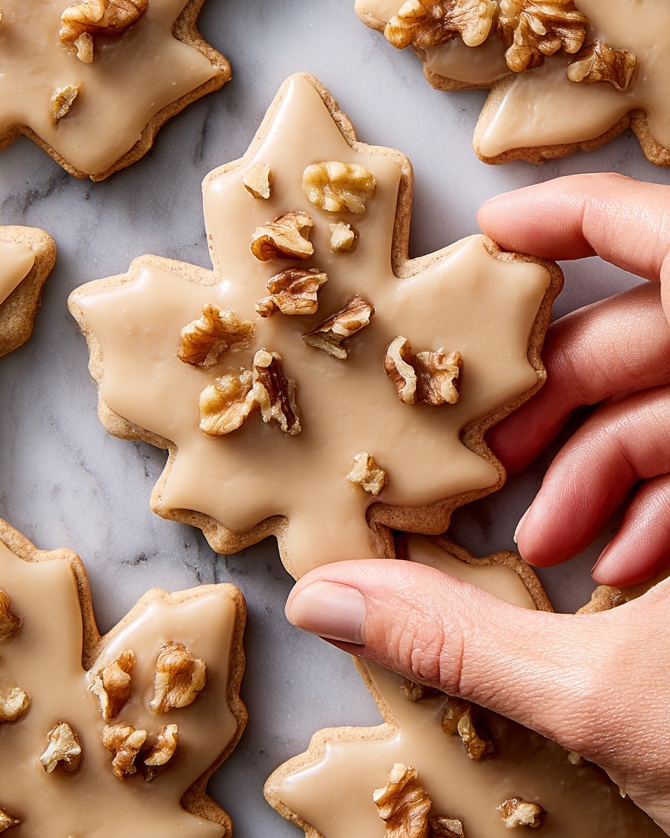 This image shows several maple leaf-shaped cookies arranged on a white marbled surface. Each cookie has one layer of smooth, light brown icing with a matte finish covering the whole cookie. On some of the cookies, small pieces of chopped nuts are sprinkled over a part of the icing, mostly near the top right or center of each cookie. The cookies have a slightly crisp edge, and the light reflects softly on the icing, giving a gentle shine. photo taken with an iphone --ar 4:5 --v 7