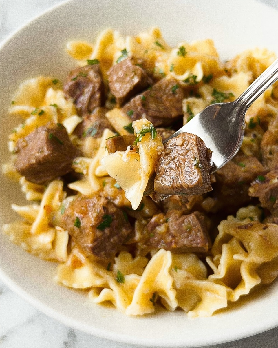 A close-up image shows a white plate filled with short pasta with ruffled edges mixed with brown pieces of meat in a light brown sauce. The pasta looks soft and slightly shiny, while the meat chunks appear tender with some texture visible. There is a silver fork holding up a piece of meat and pasta, and a woman’s hand is gently holding the fork. The background is a white marbled surface. The overall feel is warm and hearty. photo taken with an iphone --ar 4:5 --v 7