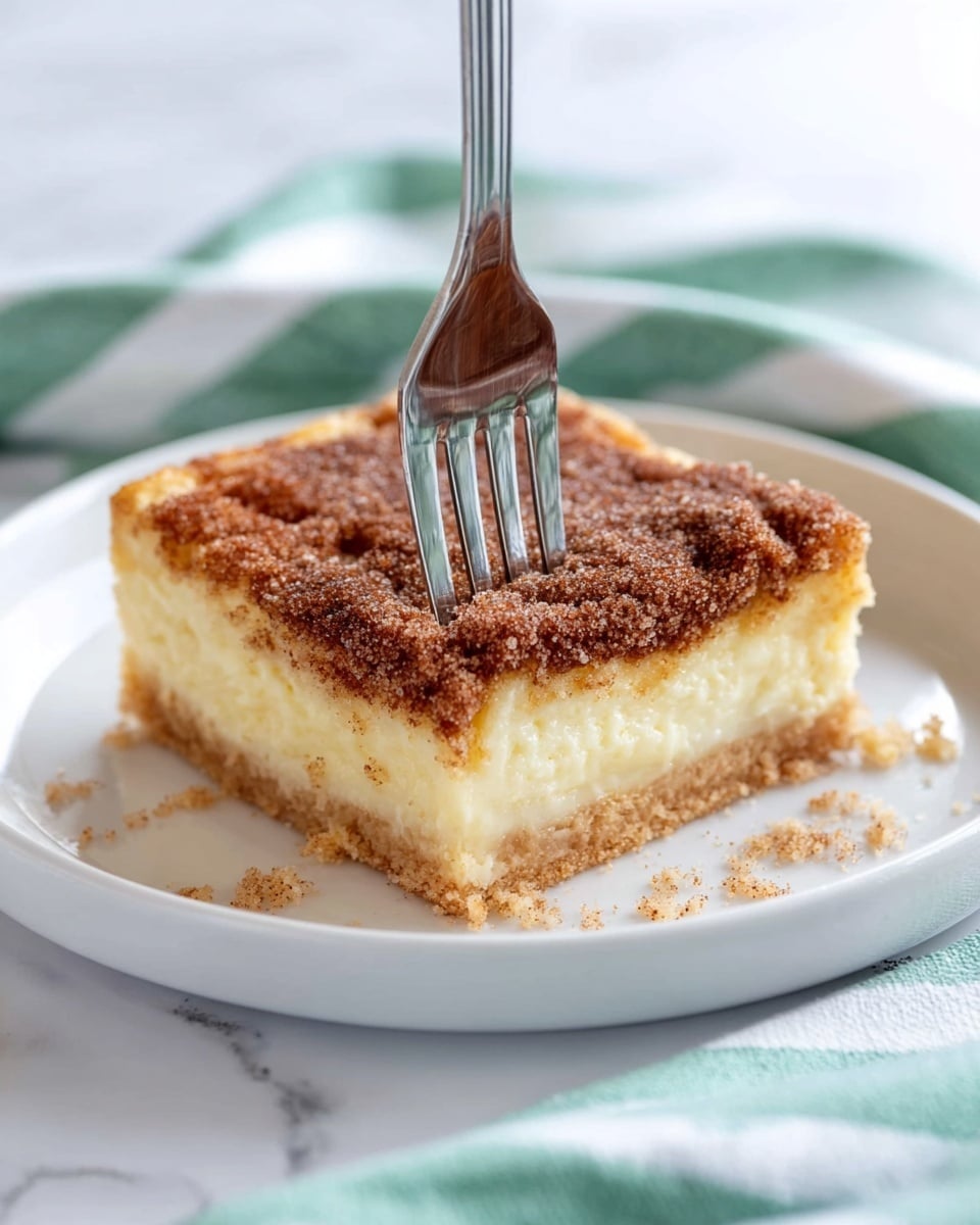 Einfaches, schmackhaftes Dessert zum Beeindrucken 1 Das Bild zeigt drei gestapelte quadratische Dessertstücke auf einer weiß marmorierten Oberfläche. Jedes Stück besteht aus zwei Hauptschichten: einer cremefarbenen hellgelben Mittelschicht und einer hellbraunen Kruste am unteren Rand. Die oberste Schicht ist eine dicke, raue Mischung aus Zimt und Zucker mit einer dunkelbraunen, körnigen Optik. Das obere Stück hat einen kleinen Biss aus einer Ecke, der die weiche cremige Schicht im Inneren freigibt. Die Ränder des Desserts sind uneben und krümelig. Foto aufgenommen mit einem iPhone --AR 4:5 --V 7