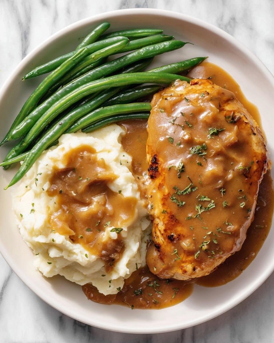A white plate on a white marbled surface holds a meal made of three parts: on the left, a pile of bright green, smooth-textured green beans stacked neatly; in the middle and right, a large piece of golden-brown cooked chicken covered in thick, brown gravy with visible small herb bits on top; next to the chicken, a large serving of creamy white mashed potatoes with soft folds, also topped with the same thick brown gravy mixed with small chunks and sprinkled with green herbs. Photo taken with an iphone --ar 4:5 --v 7
