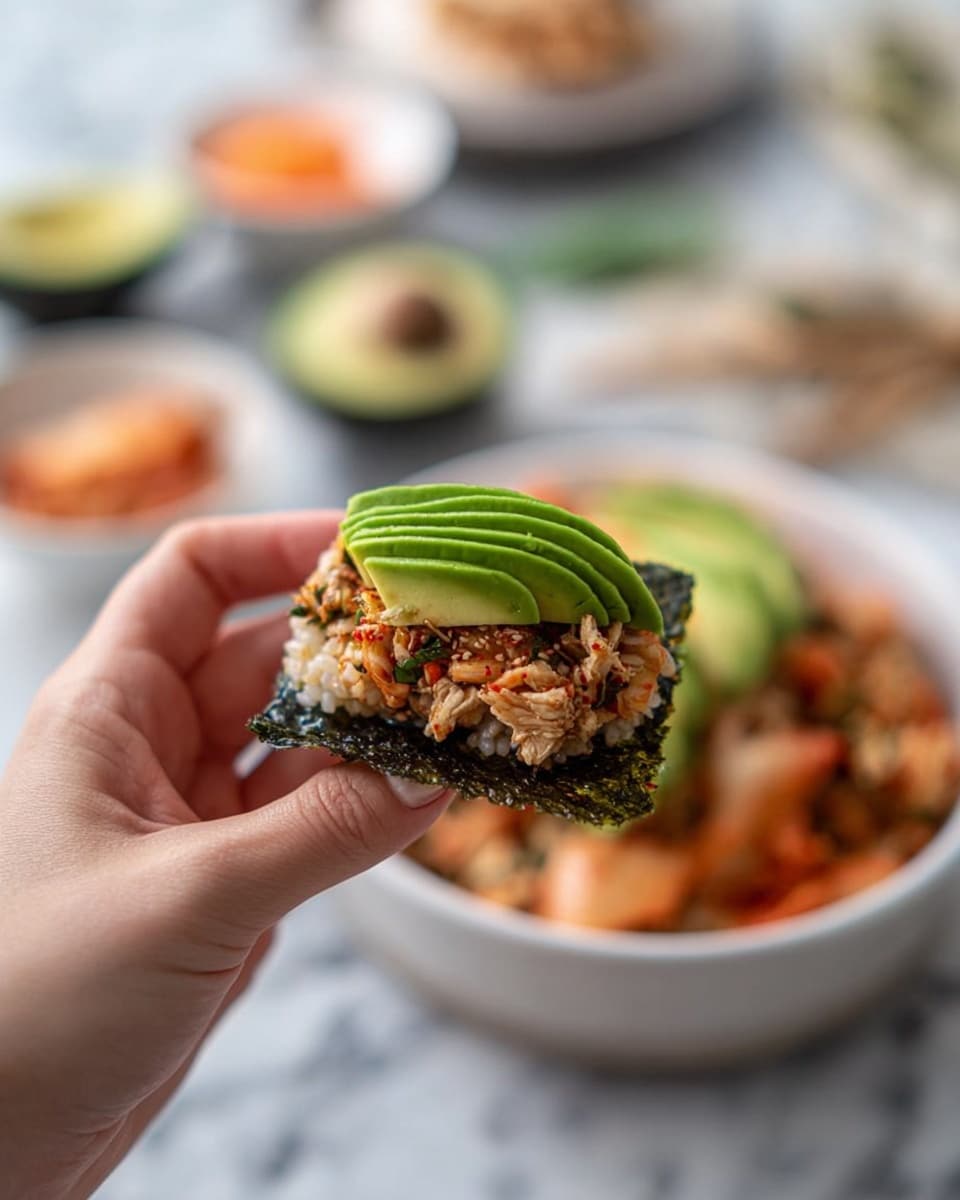 A white round bowl filled with a mix of light pink and white rice topped with a sprinkle of dark green seasoning, and a fan of bright green avocado slices placed on one side of the bowl. The bowl is set on a white marbled surface surrounded by small white dishes holding light brown powder, dark green seaweed sheets, and red-orange kimchi. A white plate with a piece of cooked pink fish and a gray cloth napkin are also visible. Photo taken with an iphone --ar 4:5 --v 7