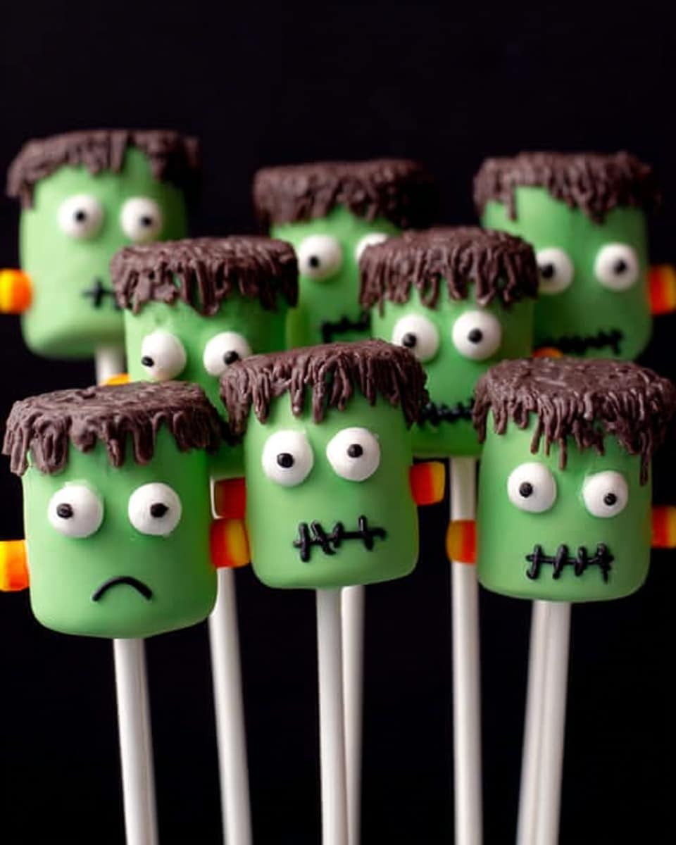 This image shows seven green marshmallow pops designed like little Frankenstein heads on white sticks. Each marshmallow is coated in smooth green icing with a rough, textured layer of brown chocolate on top, resembling hair. They all have two round white candy eyes with black pupils placed near the top center. There is a small orange candy on each side of the marshmallows to look like bolts. Each face has a tiny red zigzag scar on one side of the forehead and a wavy black line below the eyes as the mouth. The background is plain black. photo taken with an iphone --ar 4:5 --v 7