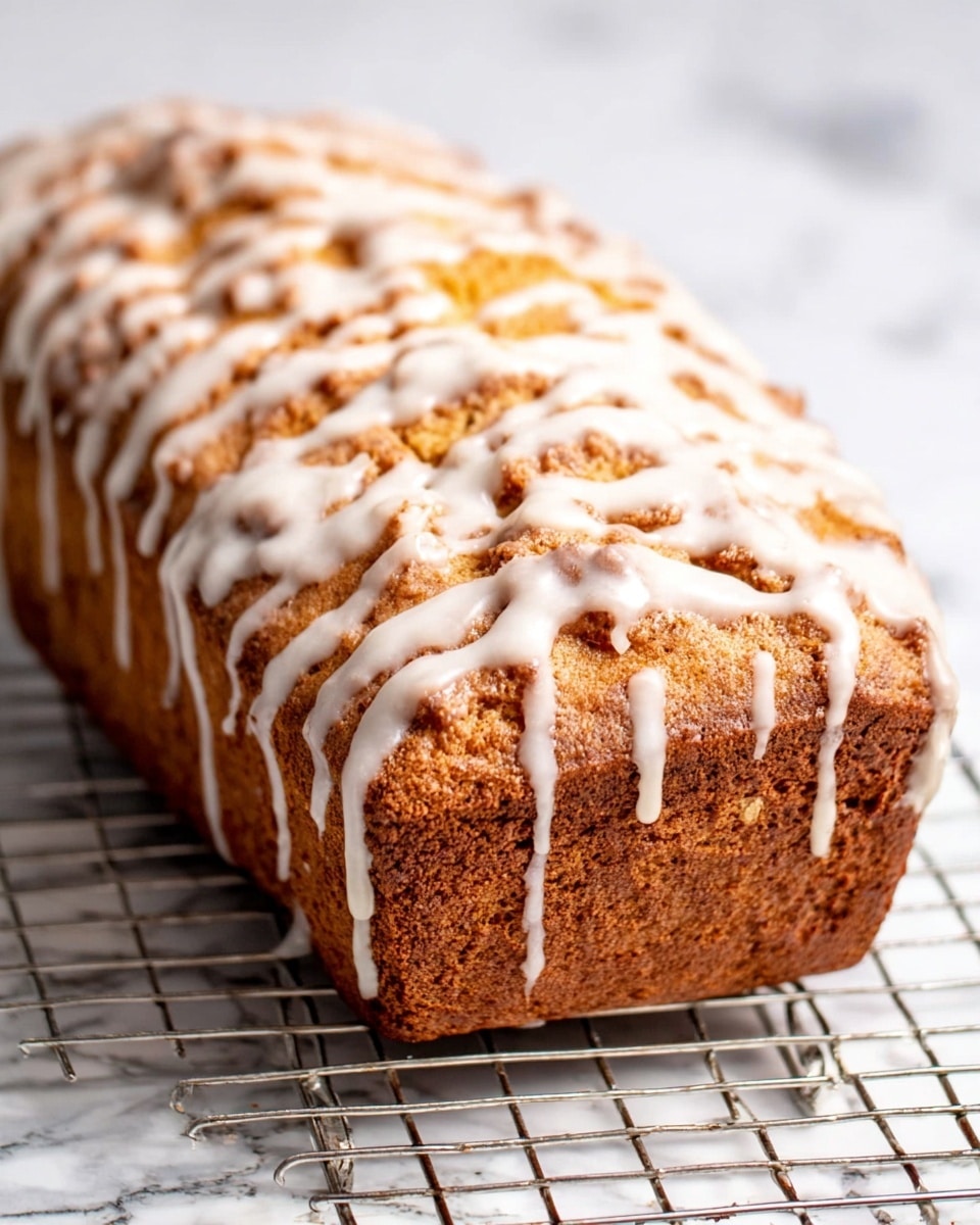 The image shows a close-up of a single slice of cinnamon swirl cake, with an orange-brown base color and a dark brown spiral cinnamon layer running through the middle. The texture looks moist and soft with a slightly crumbly edge. The slice is placed on a silver cooling rack with a white marbled surface underneath. Part of the whole loaf with a glazed outer crust is visible at the top right corner and the bottom side of the image, showing a rough texture with a shiny white glaze coating the crust. Photo taken with an iphone --ar 4:5 --v 7