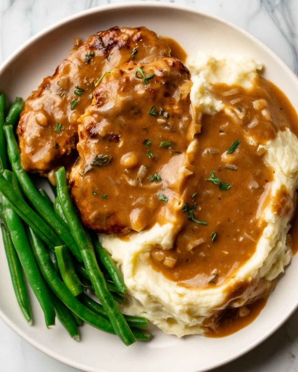 The dish shows two pieces of cooked chicken covered in a thick brown gravy with visible small herbs on top, placed side by side on the right side of a white plate. On the left side of the plate, there is a neat pile of bright green cooked green beans with a smooth texture. Between the chicken and green beans is a generous portion of creamy mashed potatoes that are white with a slightly lumpy texture, also covered with the same brown gravy that has small visible chunks and herbs. The plate sits on a white marbled surface. photo taken with an iphone --ar 4:5 --v 7