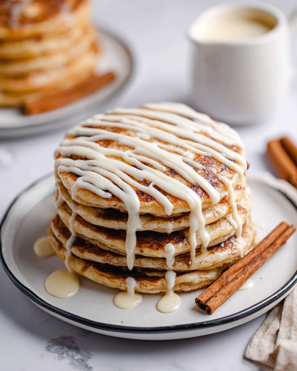 A stack of six thick pancakes sits on a white plate with a thin black rim, placed on a white marbled surface. Each pancake shows a light golden color with a dark cinnamon swirl running through the middle and across the top pancake. The stack is topped with white icing drizzled in neat, horizontal lines across the top. A metal spatula is lifting a piece of the stack, revealing the fluffy inside texture. In the background, another smaller stack of pancakes with similar white icing is slightly blurred, next to a small white jug filled with cream. Photo taken with an iphone --ar 4:5 --v 7
