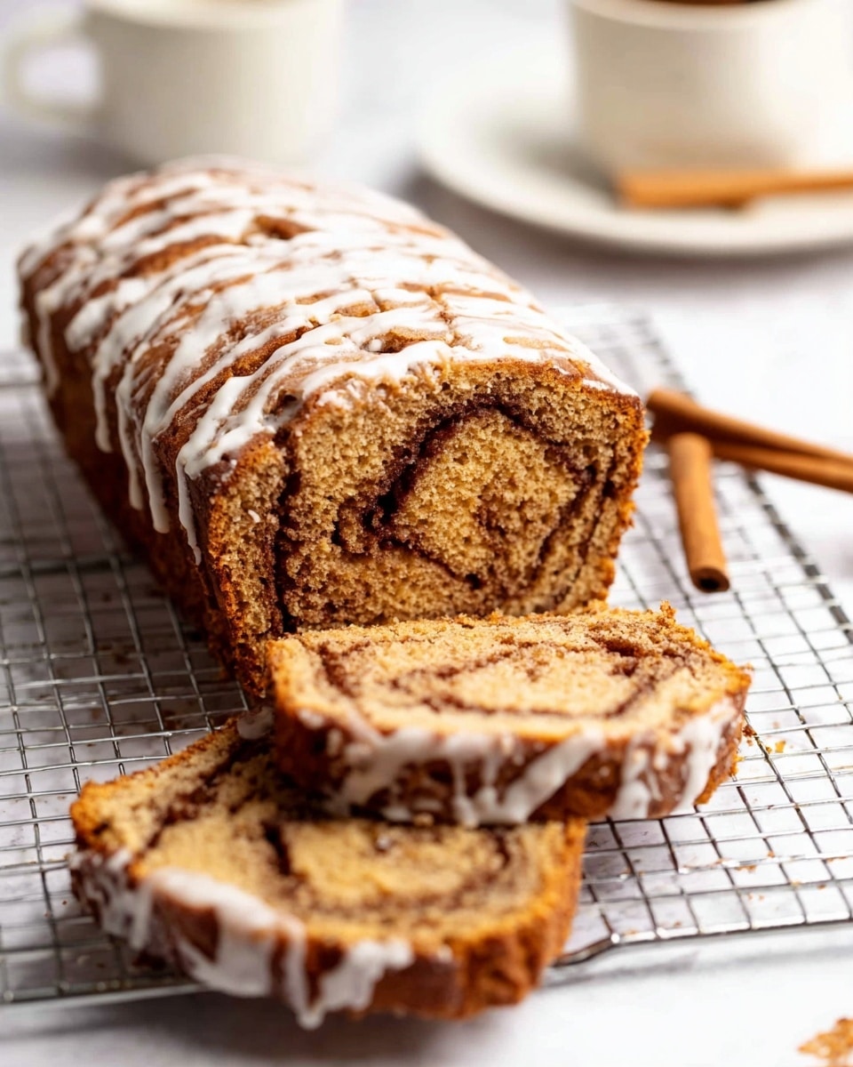 The image shows a loaf of cinnamon swirl quick bread with three layers visible in two slices resting on a wire rack. The outer crust is golden brown with a slightly rough texture, while the inside is a moist, soft light brown with darker swirls of cinnamon running through the middle. A thin white glaze is drizzled unevenly across the top and sides of the bread, creating a shiny contrast. The background is a white marbled surface with a white plate and a cinnamon stick blurred in the back. Photo taken with an iphone --ar 4:5 --v 7