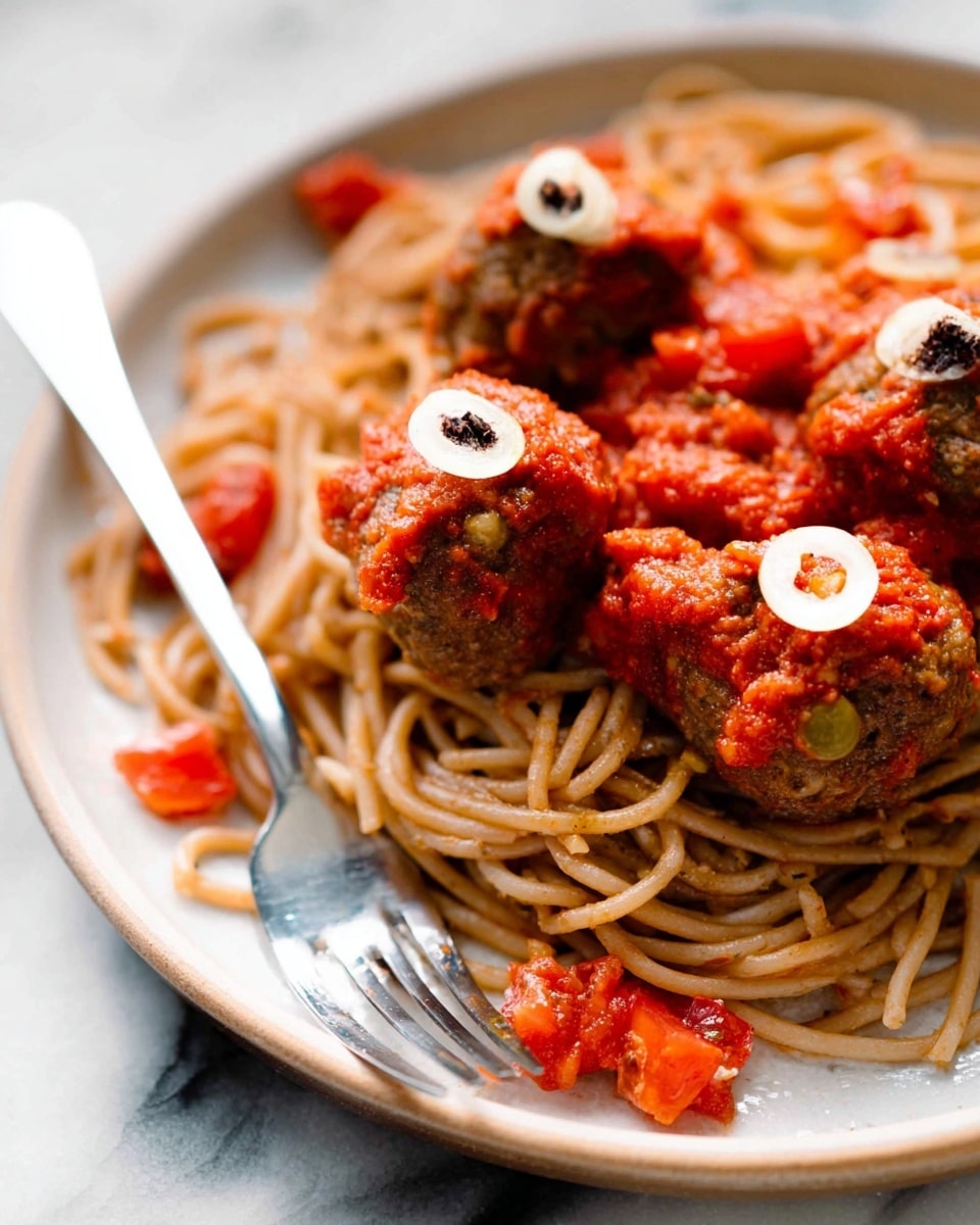 A white plate holds a nest of light brown spaghetti topped with small round meatballs. Each meatball is covered with a bright red tomato sauce and garnished with a thin white garlic slice topped with a tiny dark piece. Small chunks of tomato sauce are scattered around the spaghetti. A fork rests on the side of the plate, which sits on a white marbled surface. Photo taken with an iphone --ar 4:5 --v 7