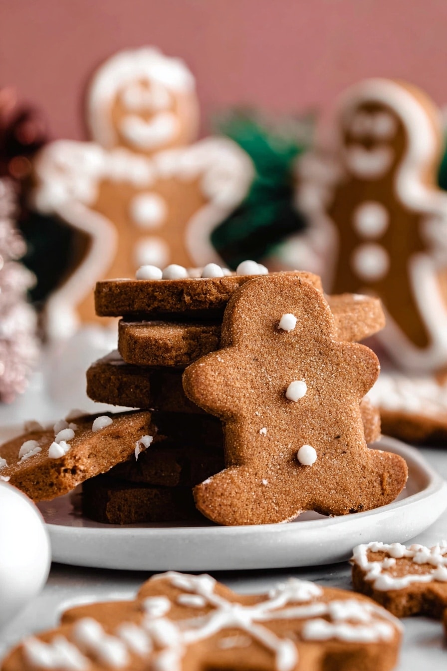 A close-up view of a stack of three brown gingerbread cookies with white icing decoration on top, placed on a white scalloped plate. The middle cookie is broken in half, showing a moist and textured inside. Around the plate, smaller gingerbread cookies with white icing details lay flat. In the background, two standing gingerbread figures with white icing decoration are blurred against a soft pink backdrop. The surface beneath the plate is a white marbled texture. Photo taken with an iphone --ar 4:5 --v 7