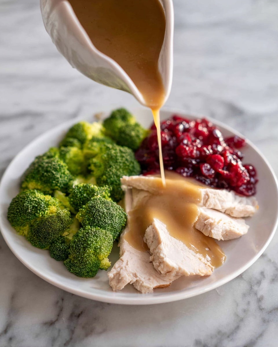 On a white plate resting on a white marbled surface, there are four slices of light beige cooked turkey layered slightly overlapping, each covered with a smooth, light brown gravy speckled with small mushroom pieces. To the left of the turkey, there are several bright green broccoli florets arranged together in a small cluster. Near the top of the turkey slices, a small bunch of fresh green parsley is placed as garnish. To the right of the turkey, there is a small serving of deep red cranberry sauce with a slightly chunky texture. Photo taken with an iphone --ar 4:5 --v 7