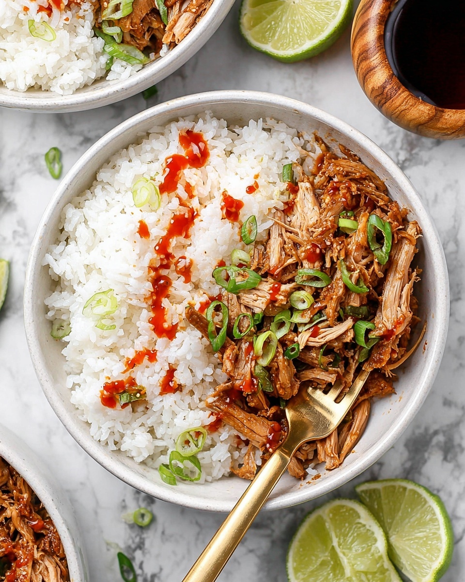 The image shows a white bowl filled with two main layers: on one side, there is soft, white rice with a light drizzle of red sauce on top, while on the other side, there is shredded cooked meat with a brown glaze, garnished with thinly sliced green onions scattered over both the meat and rice. A gold fork is placed inside the bowl, partially resting in the meat. Around the bowl, there are small wedges of lime and a wooden container holding a dark liquid. The whole scene is set on a white marbled surface. photo taken with an iphone --ar 4:5 --v 7