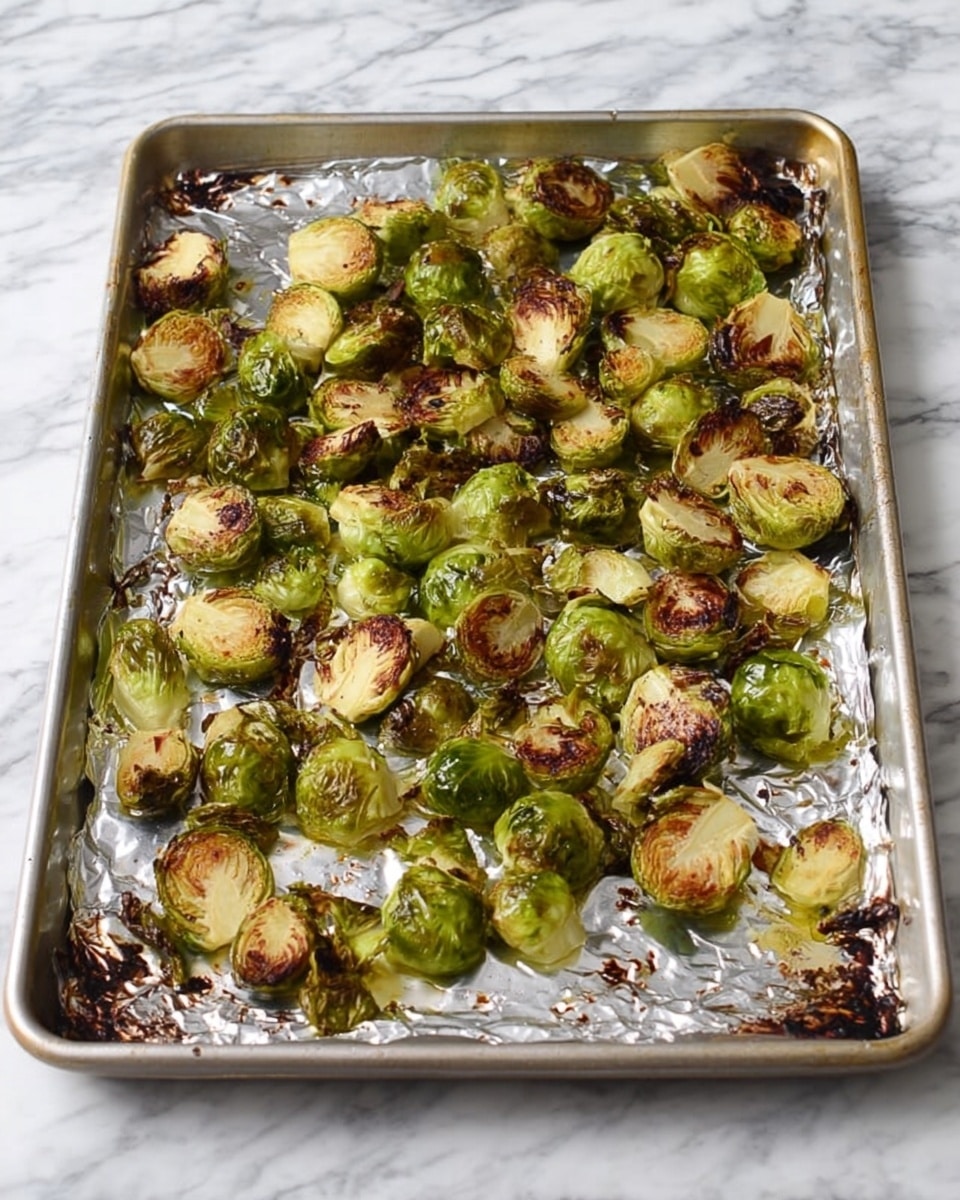 A baking sheet lined with silver foil holds a single layer of roasted Brussels sprouts cut in half, showing their bright green and golden-brown caramelized edges with some darker, crispy spots. The Brussels sprouts are scattered unevenly across the foil, with a mix of textures from tender green leaves to slightly charred brown surfaces. The baking sheet is placed on a white marbled surface. Photo taken with an iphone --ar 4:5 --v 7