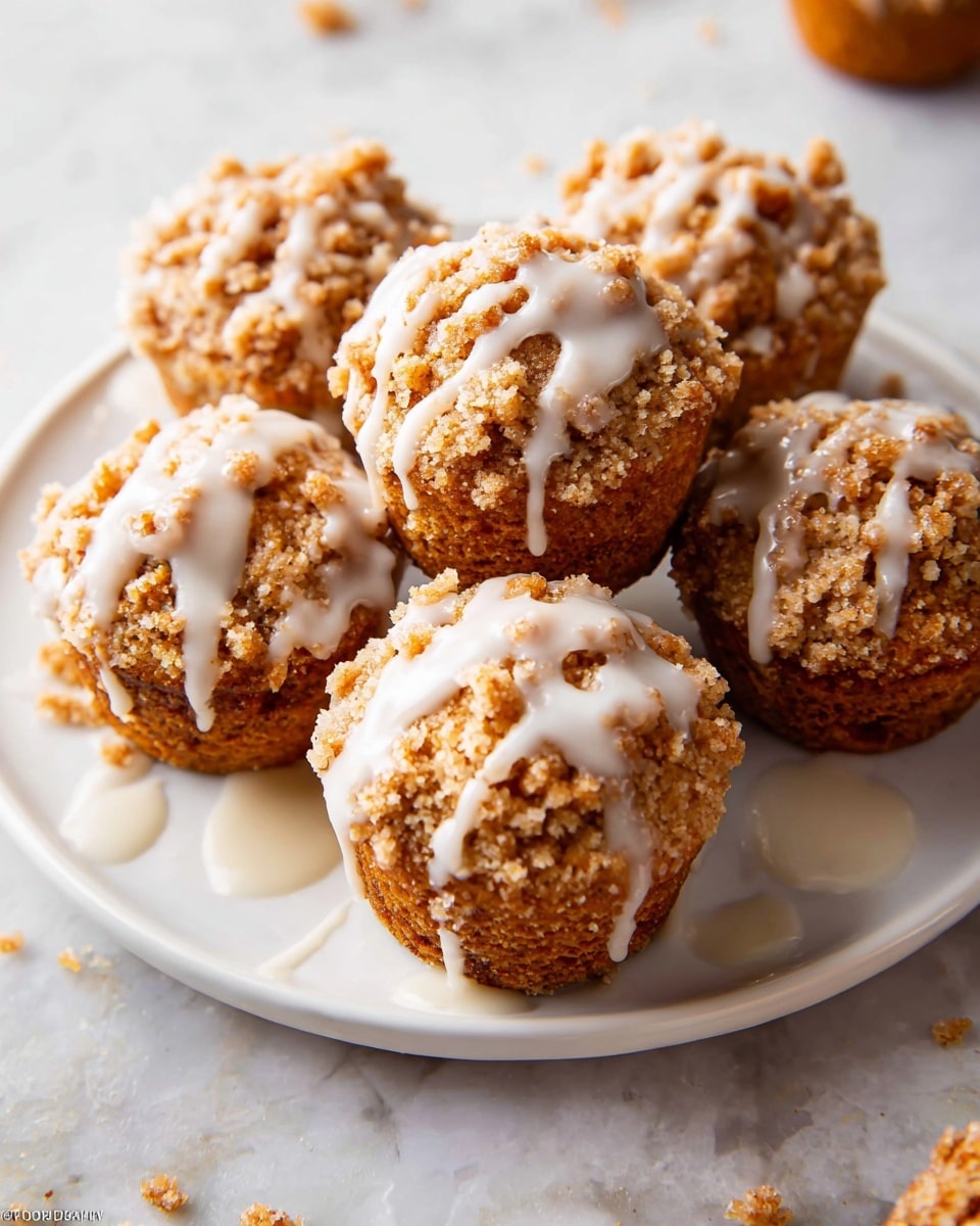 The image shows five muffins with a golden brown crumb topping and light white drizzle on top. Each muffin has a rough, crumbly texture on the top layer, sitting on a soft brown base layer wrapped in light tan paper liners. One muffin in the foreground has its crumbly wrapper gently peeled back, resting on a white marbled surface with scattered small crumbs around it. The muffins are arranged close together, softly blurred in the background to emphasize the muffin in front. photo taken with an iphone --ar 4:5 --v 7