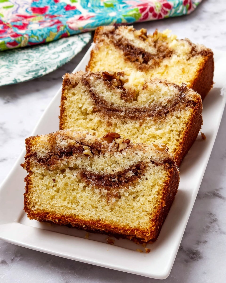 Three slices of yellow cake with a brown crumbly topping and chunks of nuts inside each slice are placed side by side on a white rectangular plate. The cake has a golden brown crust around the edges and a soft, moist inside with visible swirls of a darker filling. The plate sits on a white marbled surface with a folded cloth showing a blue and green floral pattern in the background. Photo taken with an iphone --ar 4:5 --v 7