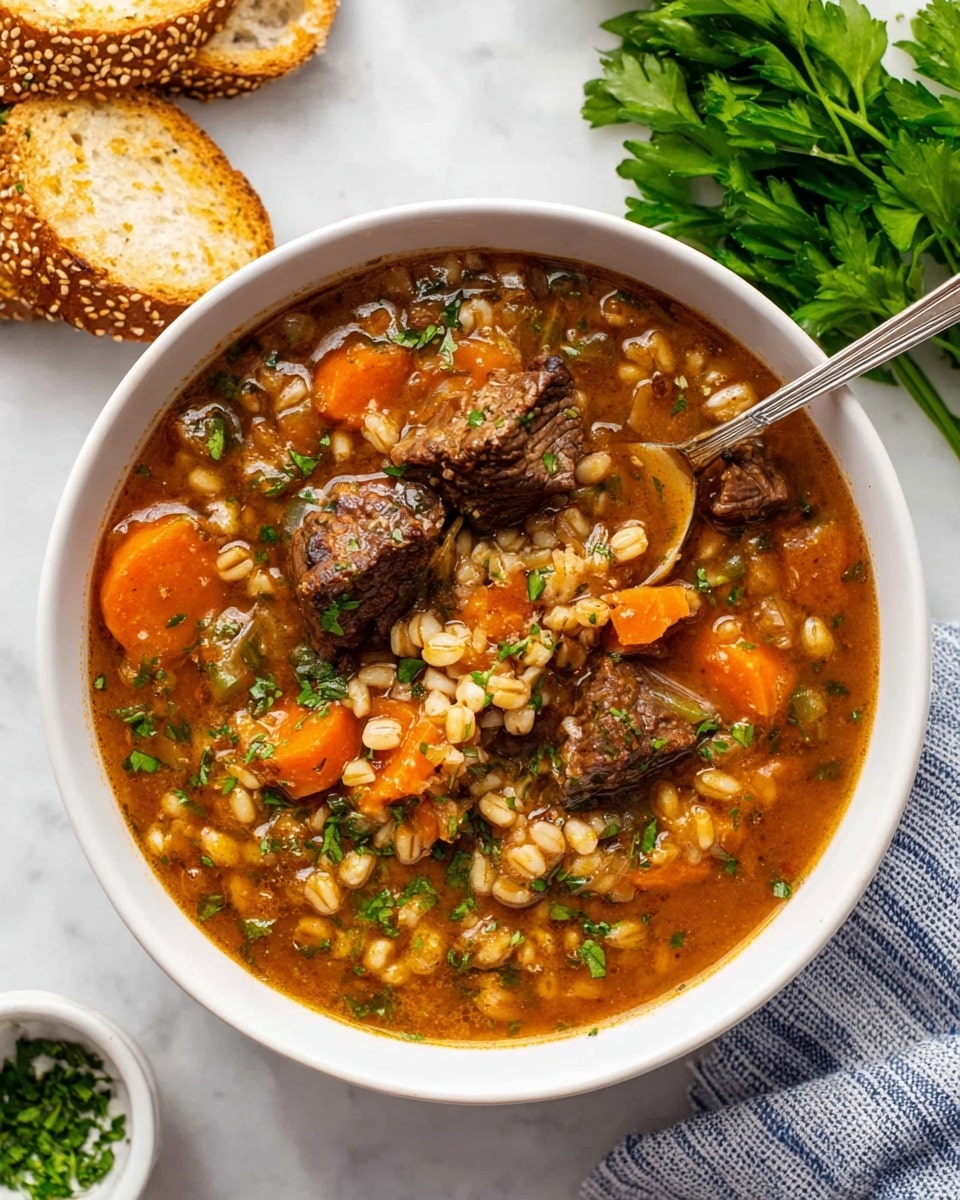 A white bowl filled with a rich brown beef and barley stew, showing several chunks of dark brown beef, orange carrot slices, and beige barley grains in a thick broth with visible bits of green herbs sprinkled throughout. A silver spoon rests in the bowl, holding a piece of beef, barley, and some carrots. The bowl is placed on a white marbled surface with a bunch of fresh green parsley on the top right and toasted sesame bread slices on the top left. A small white dish with chopped herbs is visible near the bottom left, and a blue and white striped cloth sits under the bowl on the bottom right. photo taken with an iphone --ar 4:5 --v 7