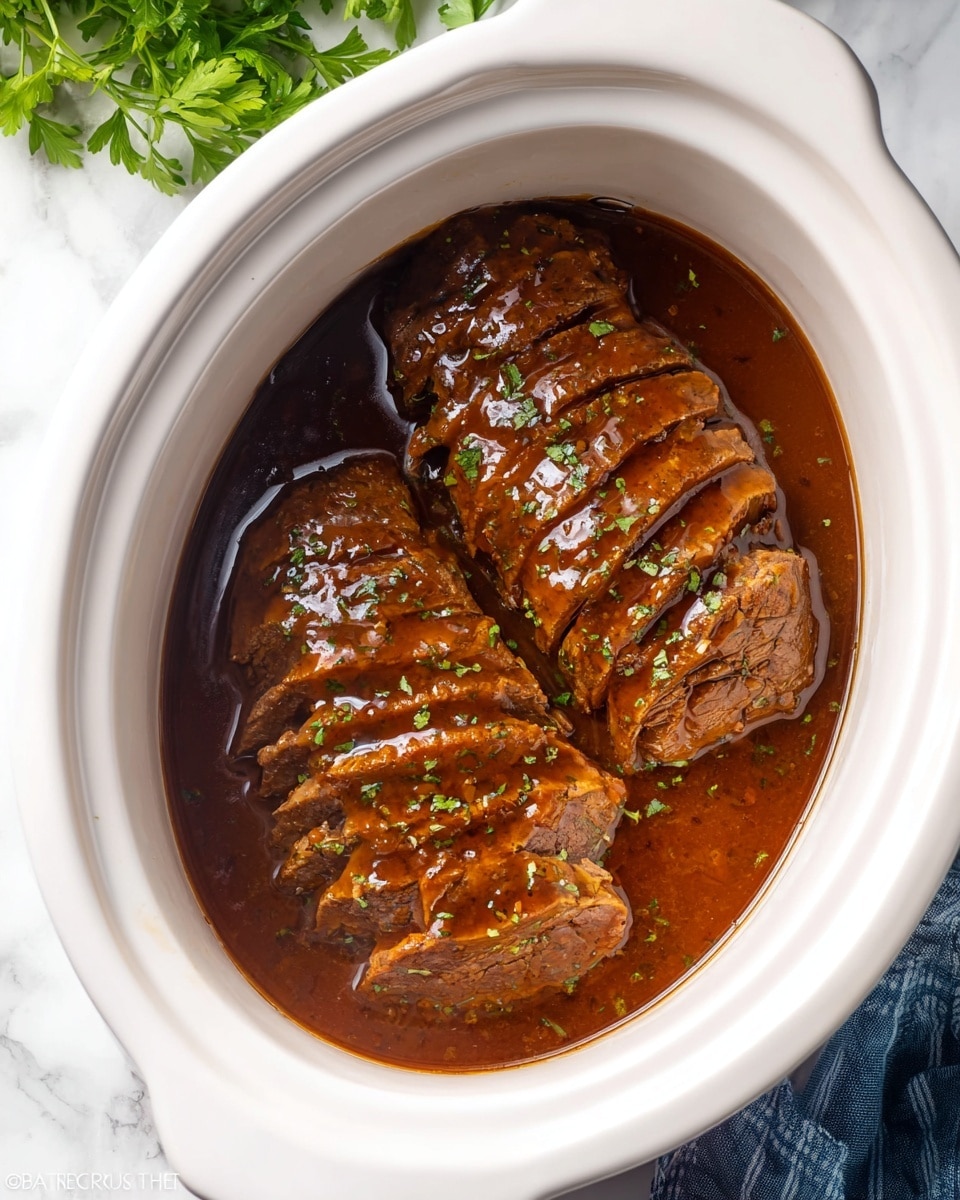 The image shows two pieces of cooked meat sliced into thick pieces, arranged side by side inside a white slow cooker. The meat is covered with a shiny, rich brown sauce, and small bits of green herbs are sprinkled lightly on top. The sauce pools around the bottom of the meat, giving a moist and glossy look. The slow cooker sits on a white marbled surface with some green leafy herbs partially visible at the top left corner and a folded blue cloth near the bottom right corner. photo taken with an iphone --ar 4:5 --v 7