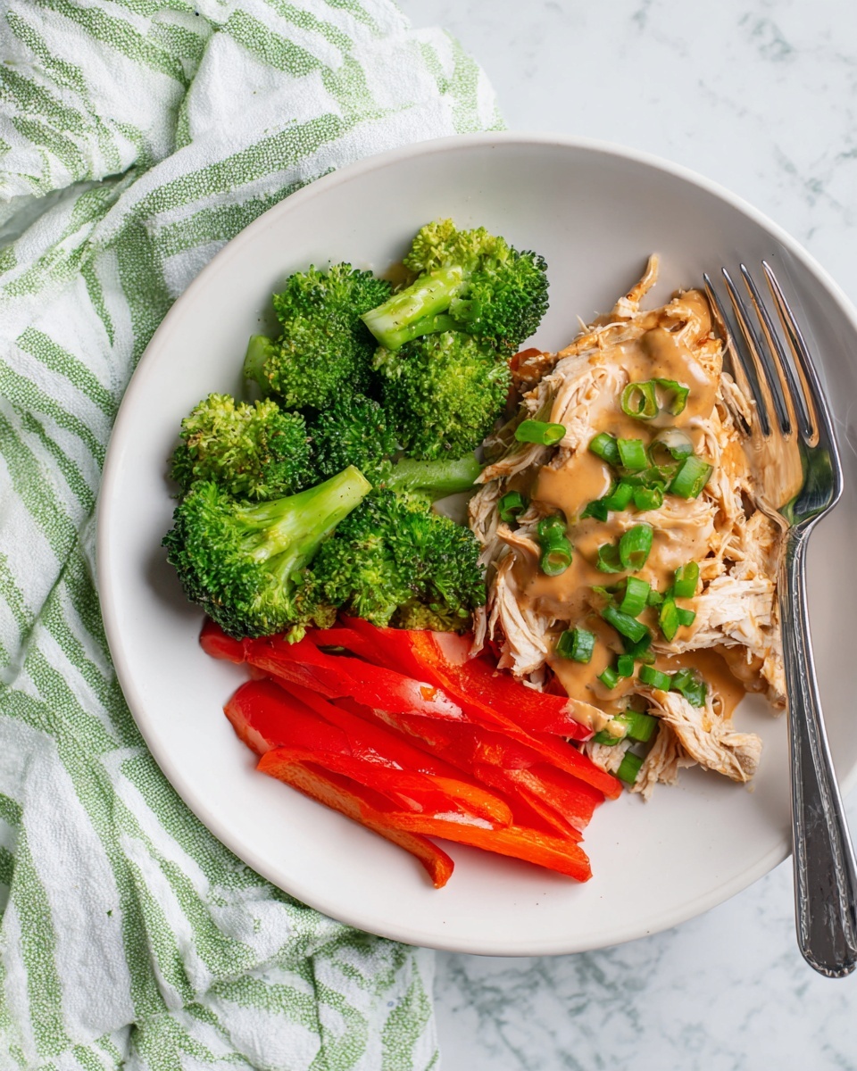 On a white plate placed on a white marbled texture with a green and white striped cloth beneath, there are three main layers of food arranged side by side. On the left, bright green broccoli florets add a rough, leafy texture. Next to the broccoli, several thin slices of fresh red bell pepper provide a smooth, shiny contrast. On the right side of the plate, there are shredded pieces of light-colored cooked chicken covered with a smooth, brown gravy sauce spread unevenly on top. Scattered on the chicken and peppers are small bits of chopped green onions adding a fresh touch. A silver fork rests on the right edge of the plate. Photo taken with an iphone --ar 4:5 --v 7