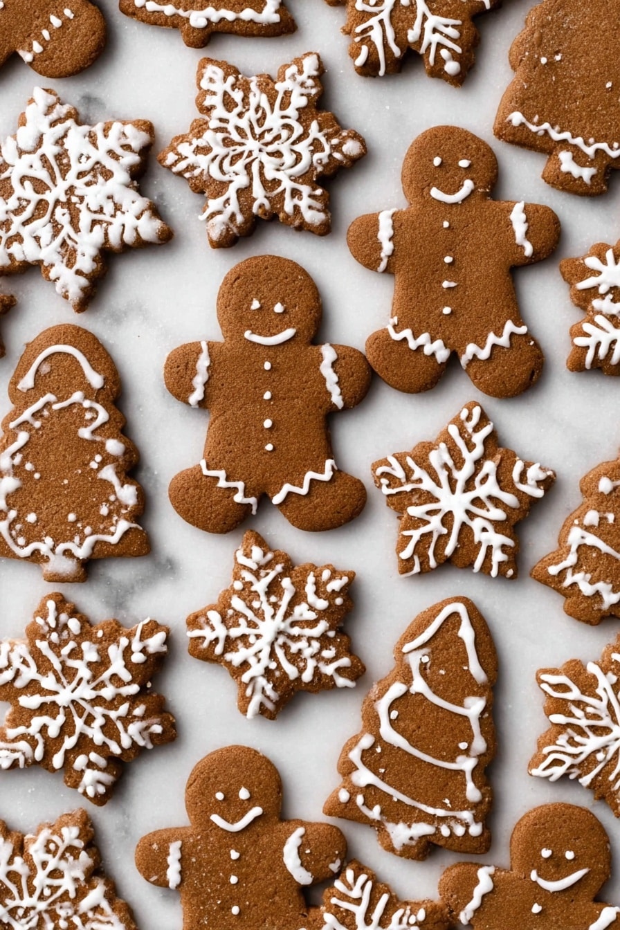The image shows a spread of gingerbread cookies on a white marbled surface. There are several gingerbread men with simple white icing outlining their arms, legs, and buttons, and some gingerbread girls decorated similarly with white icing dresses. Alongside them are snowflake-shaped cookies decorated with detailed white icing patterns that look like snowflake arms, and a few star-shaped cookies also decorated with white icing in snowflake designs. There is one large white icing decorated gingerbread Christmas tree, and a few mitten-shaped cookies with white icing lines. The cookies have a rich brown color with a slightly rough texture, and the white icing contrasts sharply on top. photo taken with an iphone --ar 4:5 --v 7