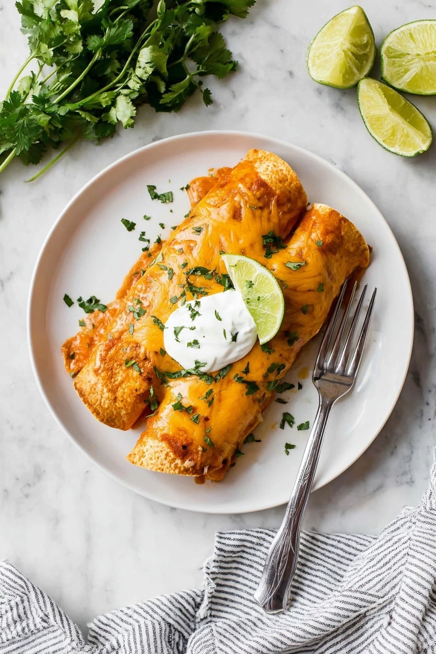 Cheesy Chicken Enchiladas Recipe 3 On a white plate, there are two rolled enchiladas covered with orange-red sauce and melted cheese, sprinkled with chopped green cilantro. On top of the enchiladas, there is a dollop of white sour cream with more cilantro sprinkled over it, and a wedge of lime rests on one side. A silver fork is placed on the right side of the plate. Around the plate, there are additional lime wedges and fresh cilantro, all set on a white marbled surface with a striped cloth at the bottom right corner. photo taken with an iphone --ar 4:5 --v 7