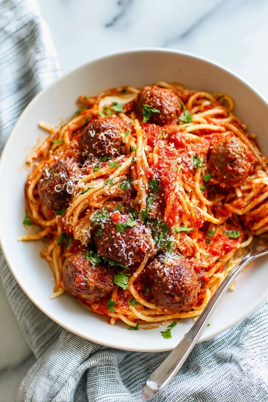 Easy Baked Meatballs with Spaghetti Recipe 6 A white bowl contains a serving of spaghetti layered with bright red tomato sauce. There are five brown meatballs placed on and around the spaghetti, each covered in sauce. The pasta is sprinkled with small green basil pieces and grated white cheese. A fork rests on the left side inside the bowl. The dish is set on a white marbled surface with a blue and white striped cloth partially visible in the background. Photo taken with an iphone --ar 4:5 --v 7