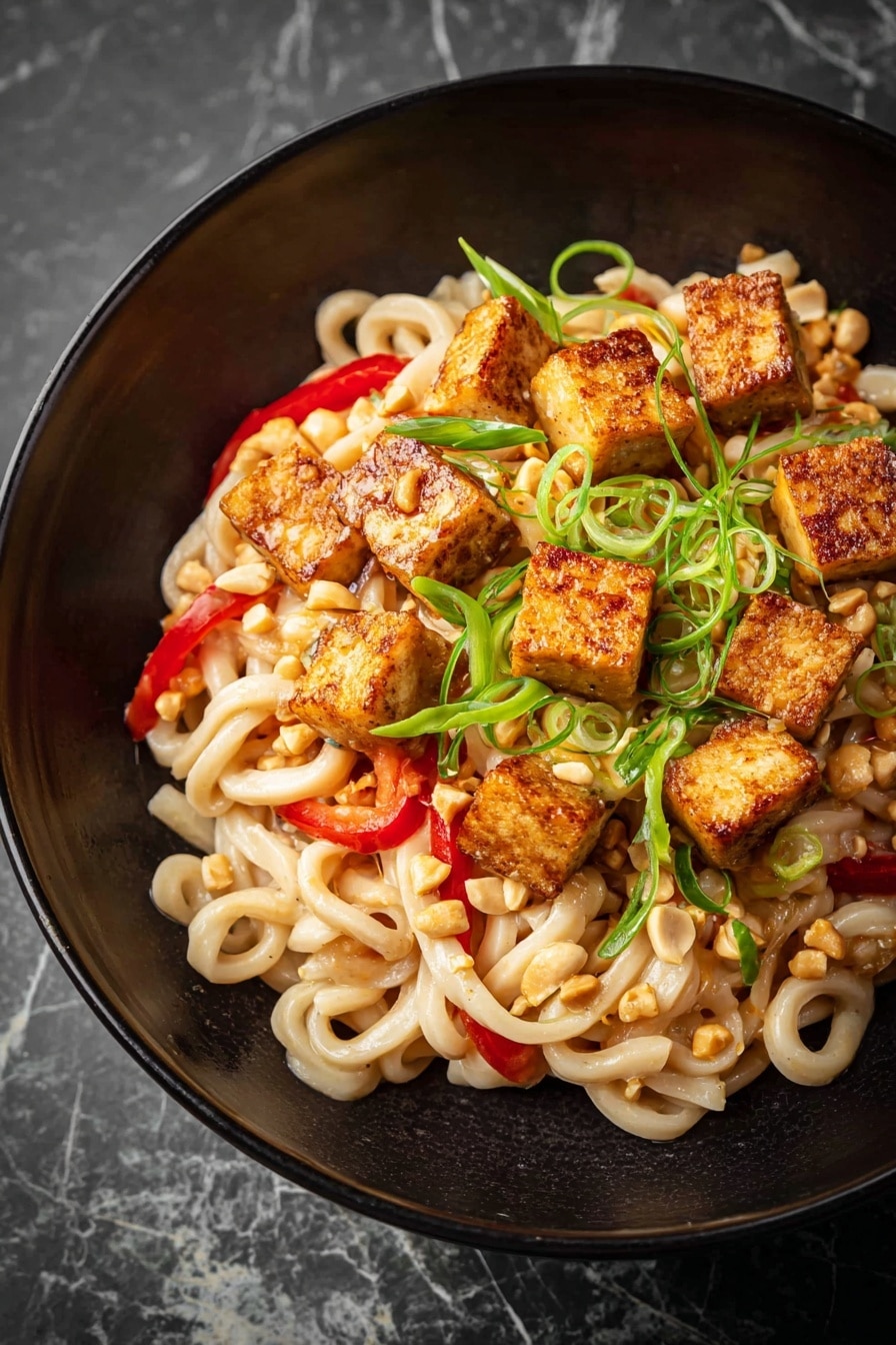 Garlic Peanut Noodles Recipe 5 The image shows a white bowl filled with thick, creamy noodles twisted together, coated in a light beige sauce with a slightly glossy texture. Mixed throughout the noodles are thin green vegetable strips and bits of crushed peanuts scattered on top, adding texture and contrast. There are small red chili flakes sprinkled over the dish, providing a pop of color. A woman's hand uses light brown wooden chopsticks to lift a small tangle of noodles and vegetables, highlighting the sauce's creaminess on the strands. The bowl is placed on a white marbled textured surface with a blurred white bowl in the background. photo taken with an iphone --ar 4:5 --v 7