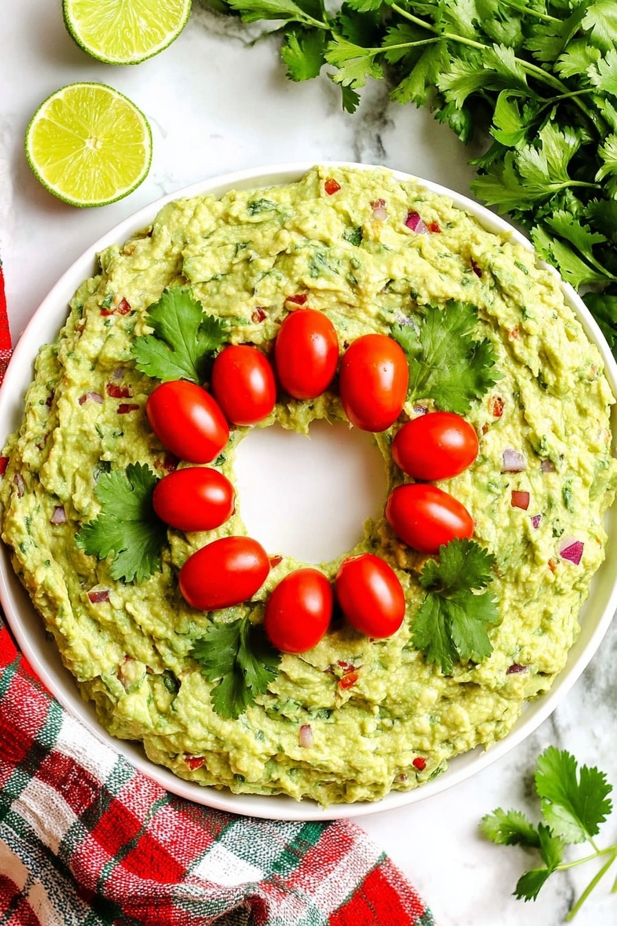A white round plate holds a thick, green guacamole ring with a hollow center, showing colorful bits of red tomatoes, purple onions, and green herbs mixed in. Three small bright red cherry tomatoes with fresh green cilantro leaves are placed in clusters on the top left, center right, and bottom left of the guacamole. The plate sits on a white marbled surface with some yellow lime halves and green cilantro sprigs beside it. A red, green, and beige plaid cloth is partly visible on the top left edge. Photo taken with an iphone --ar 4:5 --v 7