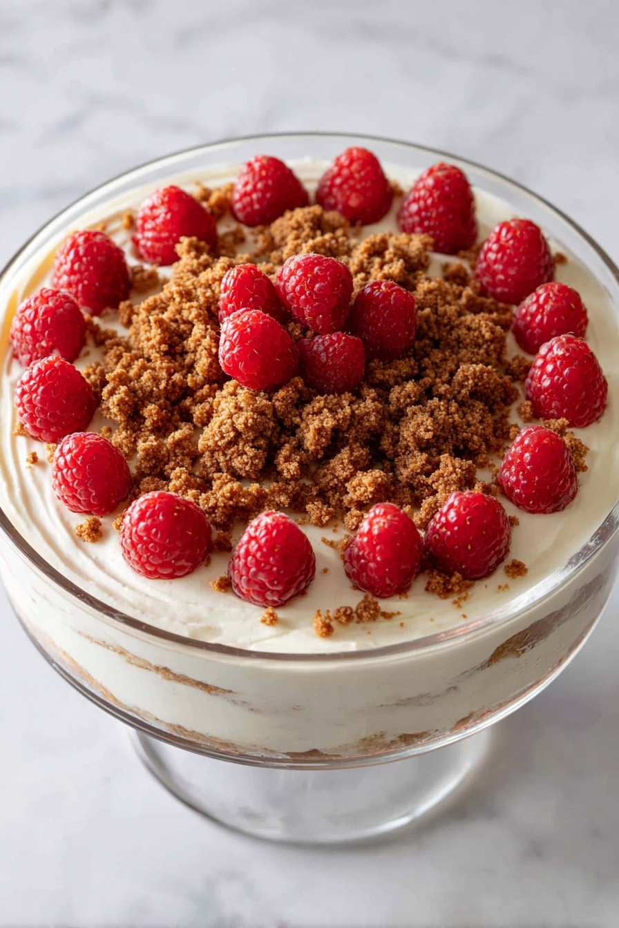 The image shows a tall clear glass bowl with a dessert made in layers. Starting from the bottom, there is a dark brown cake layer topped with a smooth pale yellow custard layer, followed by a light whipped cream layer with brown crumbs sprinkled on it. These layers are repeated once more, with the top whipped cream layer generously covered with small bright red raspberries and scattered brown crumbs around the edges. The bowl is placed on a surface with a white marbled texture, and there is a hint of blurred green pine branches in the background. photo taken with an iphone --ar 4:5 --v 7