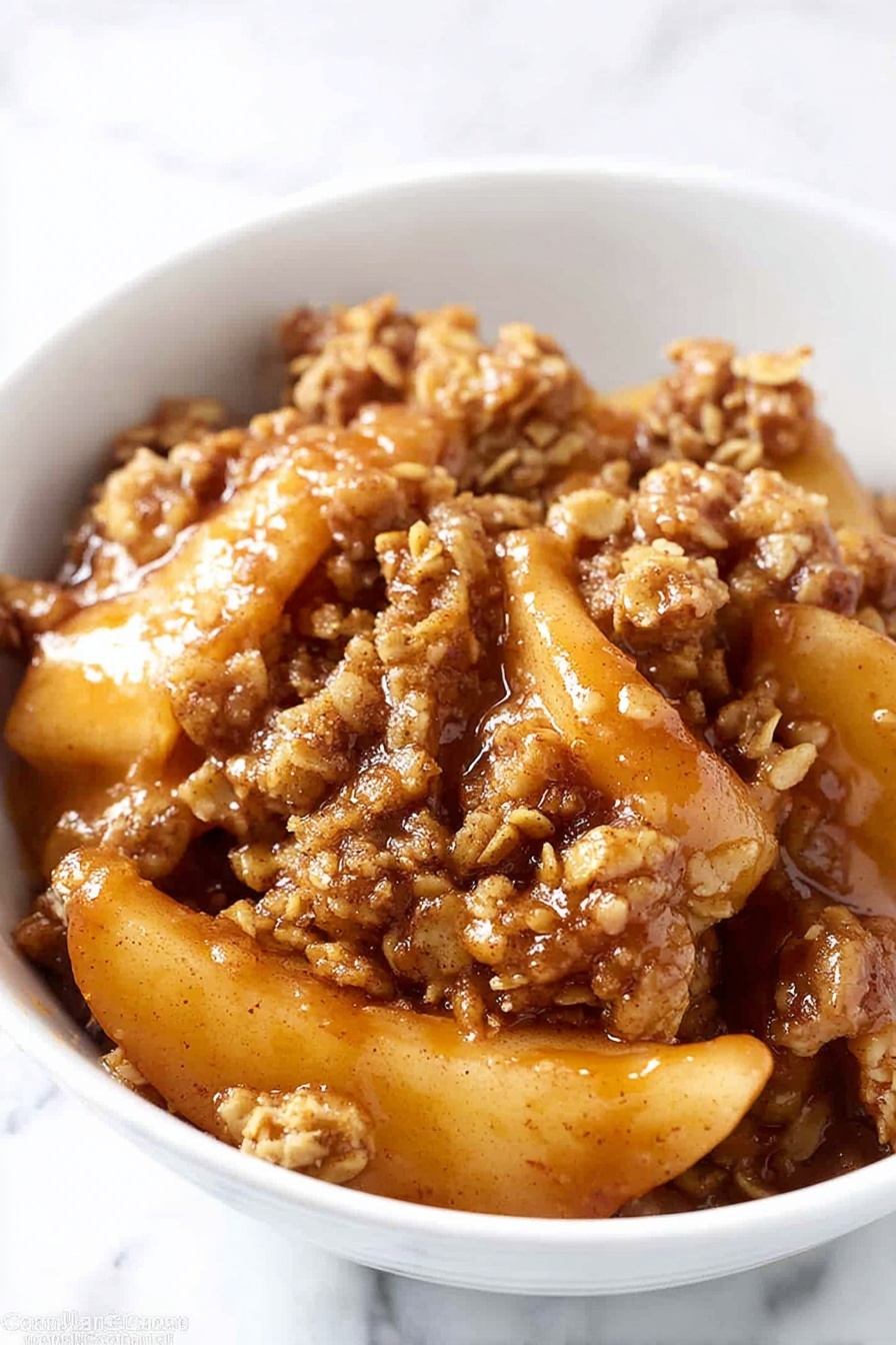 Easy Apple Crisp Recipe with Oat Topping Recipe 5 The image shows a white bowl filled with warm apple crumble dessert. At the base, there are soft, golden slices of cooked apples covered with a sticky layer of caramelized sauce. On top, there is a thick layer of golden-brown crumble made of oats and nuts, adding a rough texture. A smooth scoop of white vanilla ice cream sits on one side, melting slightly and spreading a creamy layer over the crumble and apples. A silver spoon rests inside the bowl, partly hidden behind the dessert. The bowl is placed on a white marbled surface. Photo taken with an iphone --ar 4:5 --v 7