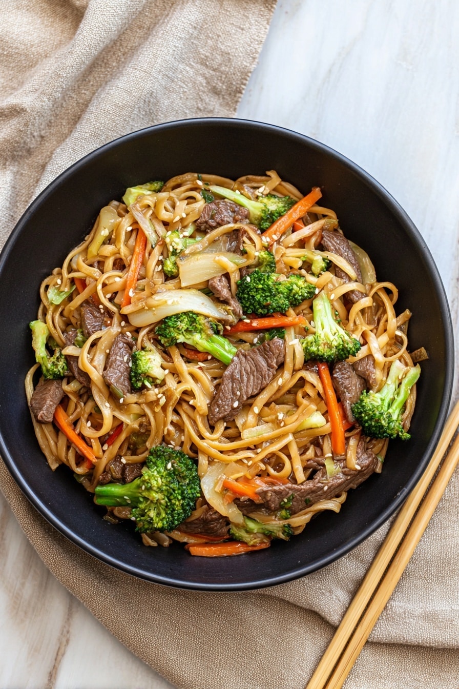 Homemade Beef Lo Mein Recipe 6 A black bowl filled with four layers of food: the bottom layer is light brown cooked noodles, the second layer has dark brown cooked beef pieces scattered evenly, the third layer contains bright green broccoli florets and thin, long, orange carrot strips mixed throughout, and the top layer is sprinkled with small white sesame seeds. The bowl sits on a white marbled surface with a beige cloth partially wrapped on one side. To the right, there is a pair of light wooden chopsticks resting beside the bowl. photo taken with an iphone --ar 4:5 --v 7