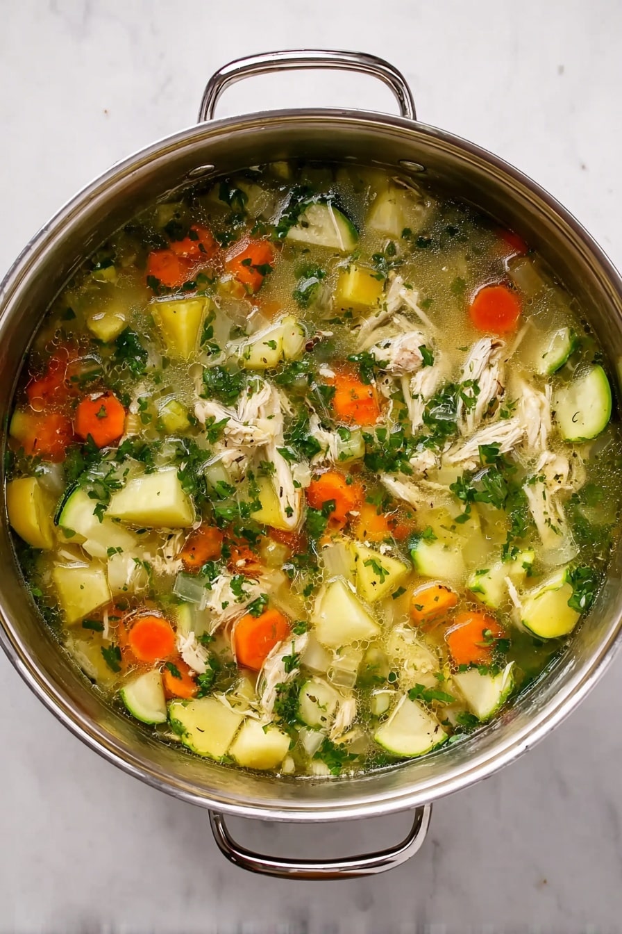 A top view of a steel pot filled with a hearty soup consisting of three main layers: at the bottom, a clear light broth with tiny oil droplets, the middle layer full of chunks of white onion and orange carrot pieces throughout, and the top layer scattered with bright green herbs and pieces of light yellow zucchini and shredded light-colored meat. The pot has two handles on either side and sits on a white marbled surface. photo taken with an iphone --ar 4:5 --v 7
