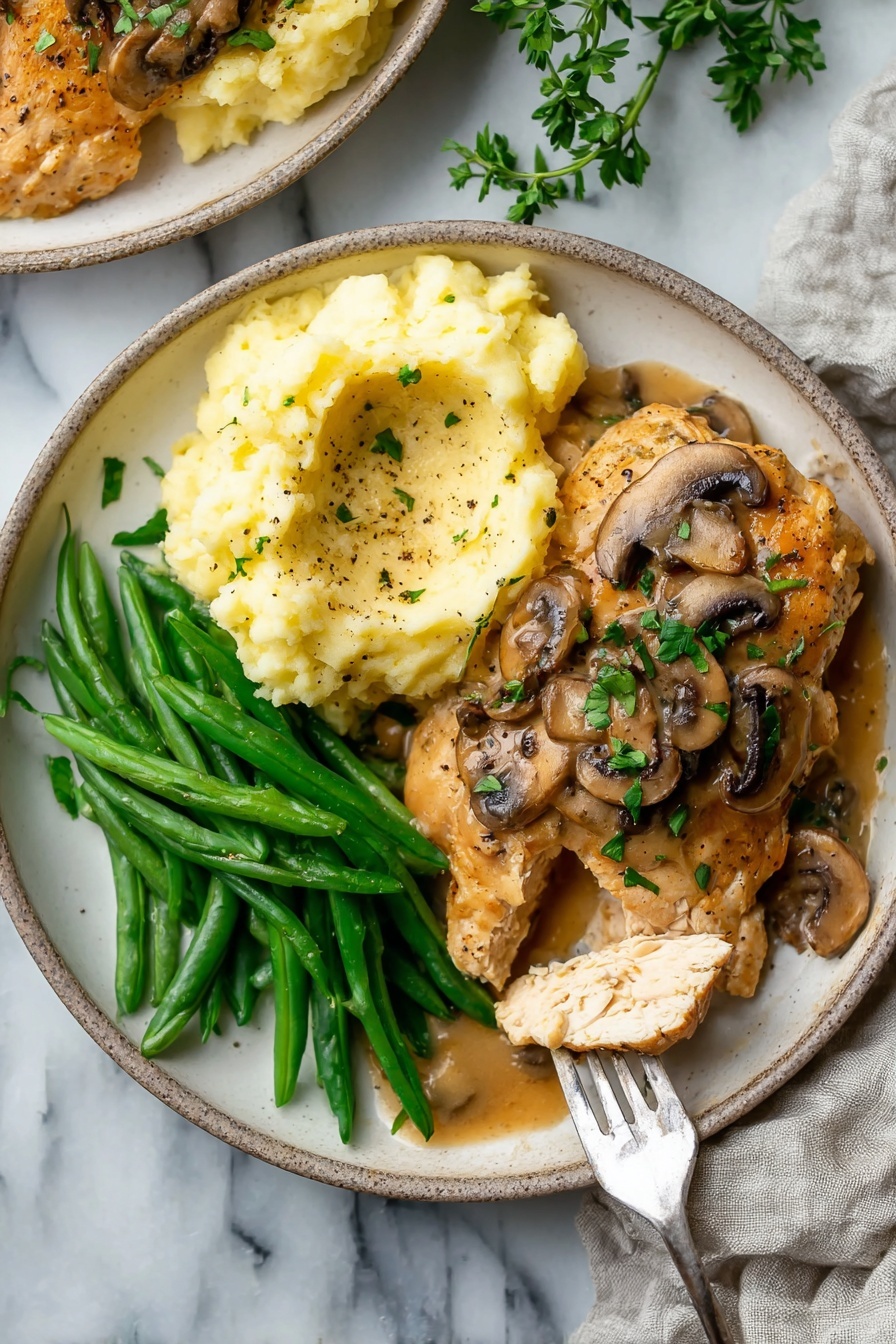 A white plate holds three main layers: on the left, bright green steamed green beans arranged lengthwise; on the right, a mound of creamy pale yellow mashed potatoes lightly speckled with black pepper and topped with a light brown gravy; and at the bottom center, a cooked chicken patty smothered with mushroom gravy that includes sliced brown mushrooms and fresh green parsley bits. A fork lifting a piece of white chicken meat is placed on the right side of the plate. The plate rests on a white marbled surface with a light-colored cloth nearby. Photo taken with an iphone --ar 4:5 --v 7