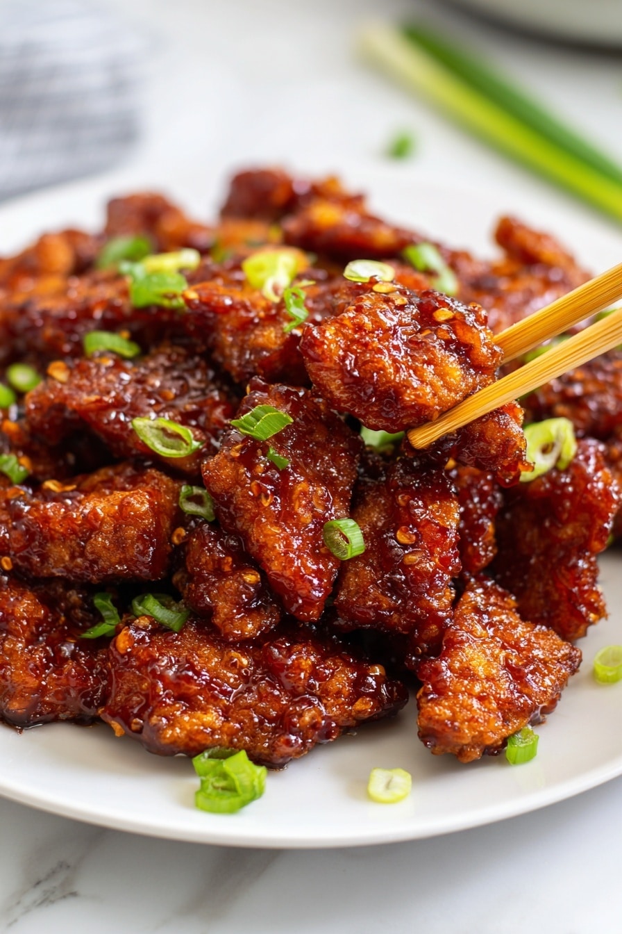 A white plate holds many small pieces of fried meat coated with a shiny reddish-brown sauce, giving a sticky and crispy look. The pieces are uneven in shape and stacked closely, with some sliced light green onions scattered on top and around the plate. In the center, a pair of light brown chopsticks picks up one piece. The plate sits on a white marbled surface with some green onion slices nearby. Photo taken with an iphone --ar 2:3 --v 7 - Crispy Chilli Chicken, spicy crispy chicken recipe, Chinese-style chicken, easy fried chicken dishes, flavorful Asian chicken