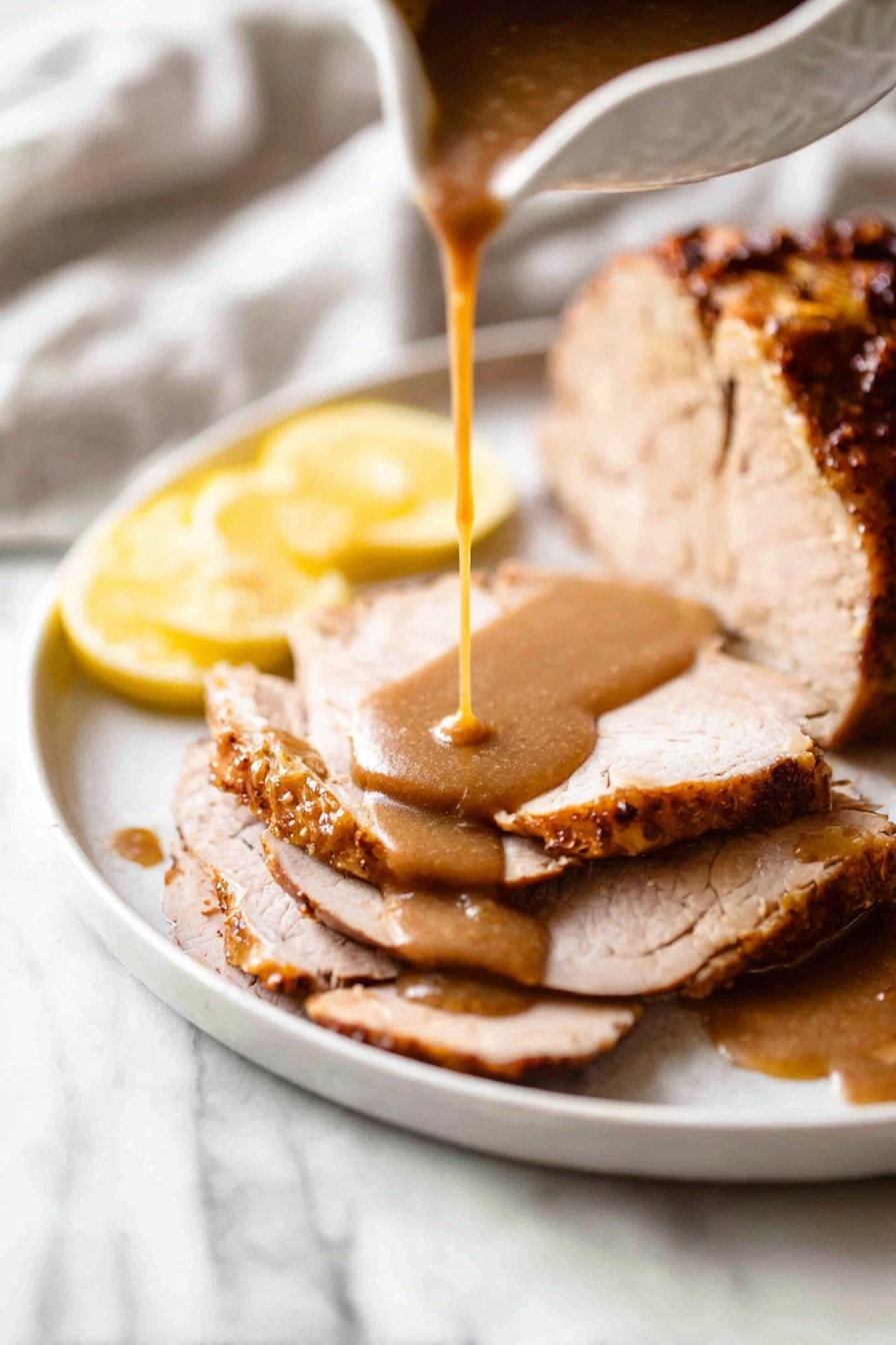 Juicy Slow Cooker Turkey Breast Recipe 8 The image shows a white plate on a white marbled surface with a large piece of cooked meat that has a golden-brown, crispy crust and some green herbs on top. To the right are four thick slices of meat, layered neatly with brown gravy drizzled over them. On the left side of the plate, there are two round lemon slices placed flat and a lemon wedge at the bottom right of the plate. Behind the plate, a white cloth holds a silver knife and fork with black handles, and to the upper left, there is a white gravy boat filled with brown gravy, with a silver spoon resting inside it. Photo taken with an iphone --ar 2:3 --v 7 - Juicy Slow Cooker Turkey Breast, slow cooker turkey, moist turkey breast, easy turkey dinner, tender turkey recipes