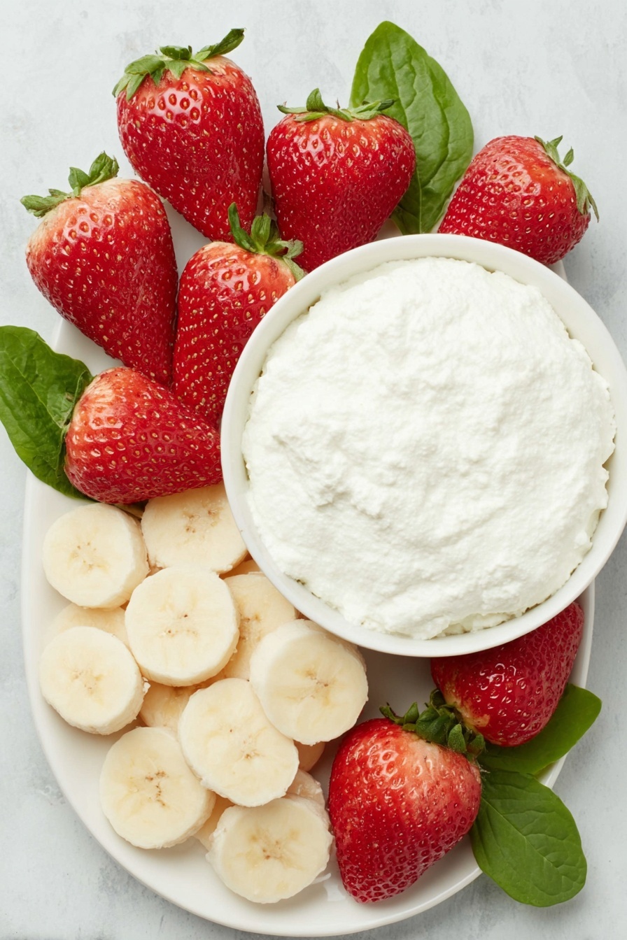 Flat lay of a dozen bright red strawberries with fresh green leaves, a ripe yellow banana sliced into round discs, a small white ceramic bowl filled with creamy white ricotta cheese, all arranged symmetrically on a clean white ceramic plate, placed on a clean white marble surface, soft natural light, photo taken with an iPhone, professional food photography style, fresh ingredients, white ceramic bowls, no bottles, no duplicates, no utensils, no packaging --ar 2:3 --v 7 --p m7354615311229779997 - Healthy Strawberry Santas, festive healthy snacks, quick holiday treats, kid-friendly fruit snacks, easy Christmas party desserts
