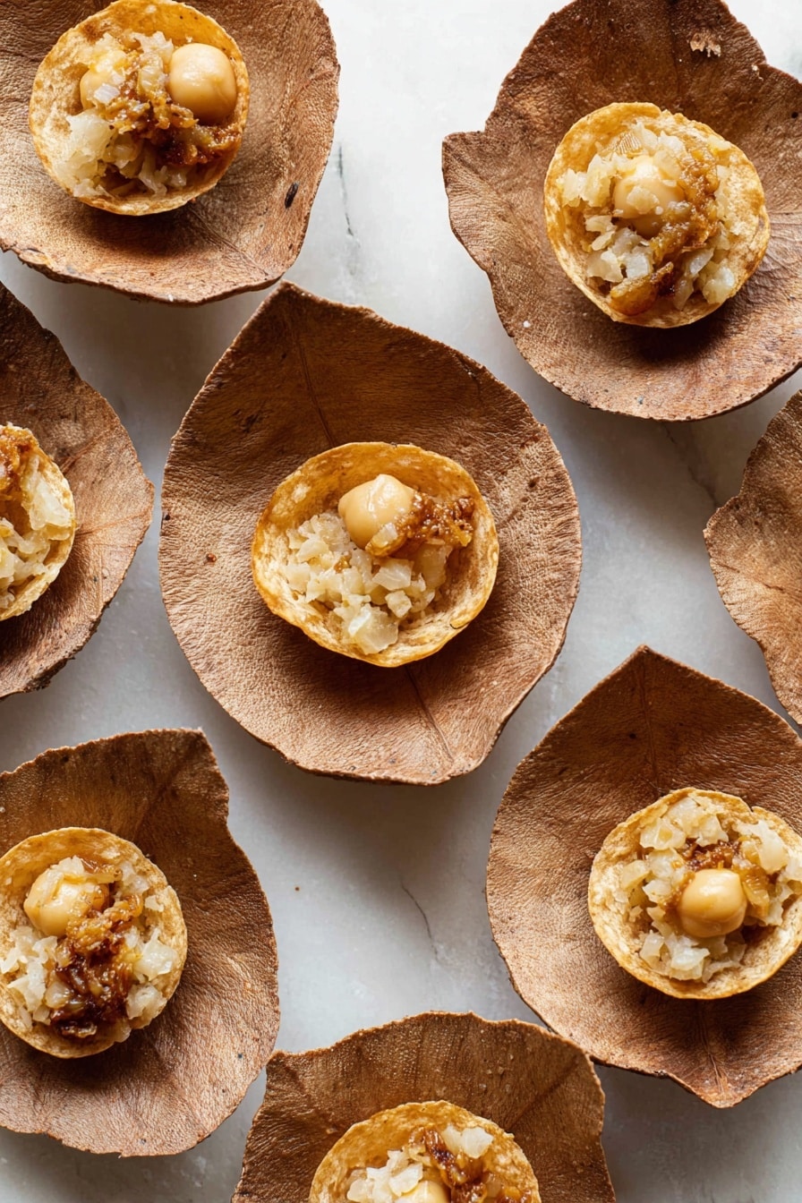Authentic Pani Puri Recipe 8 The image shows multiple small round puffed snacks placed inside brown leaf-like bowls. Each snack has a thin, crispy golden outer shell with a hollow center holding a filling made of beige and light brown small pieces, possibly chickpeas and some mashed ingredients. The bowls are arranged on a white marbled surface that contrasts with the earthy tones. The puffed snacks show a bubbling texture on their surface, and slight oil sheen is visible. photo taken with an iphone --ar 2:3 --v 7 - Authentic Pani Puri, Pani Puri recipe, Indian street food, How to make pani puri, Crispy puris and tangy jaljeera