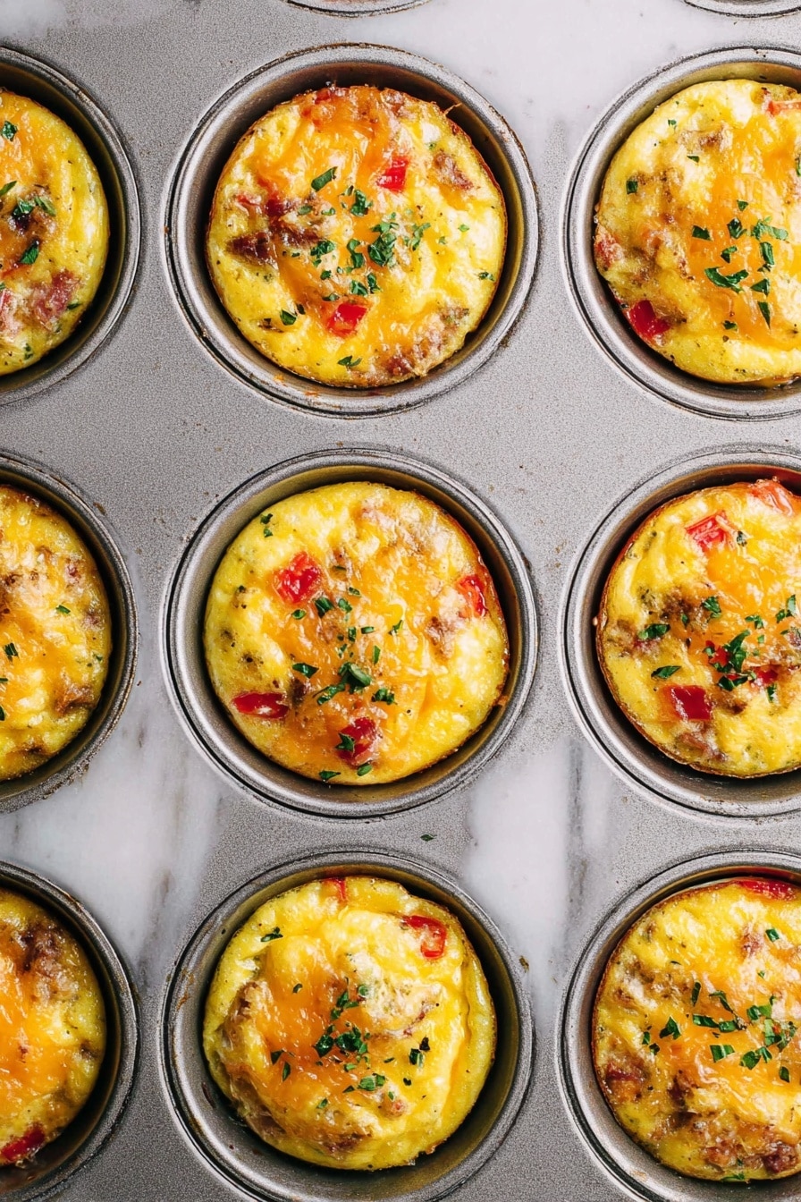 Hash Brown Egg Cups Recipe 6 The image shows a close-up of a metal muffin tray filled with nine egg muffins. Each muffin has a golden yellow base with visible pieces of red bell pepper and bits of cooked meat mixed inside. The top surface of each muffin has melted cheese bubbling and slightly browned, with small green herb leaves sprinkled on them. The tray rests on a white marbled surface, showing slight texture and wear. The egg muffins sit neatly in each round muffin cup, with even and rounded tops, each garnished similarly with herbs. photo taken with an iphone --ar 2:3 --v 7 - Hash Brown Egg Cups, breakfast egg cups, savory breakfast recipes, easy breakfast ideas, portable breakfast recipes