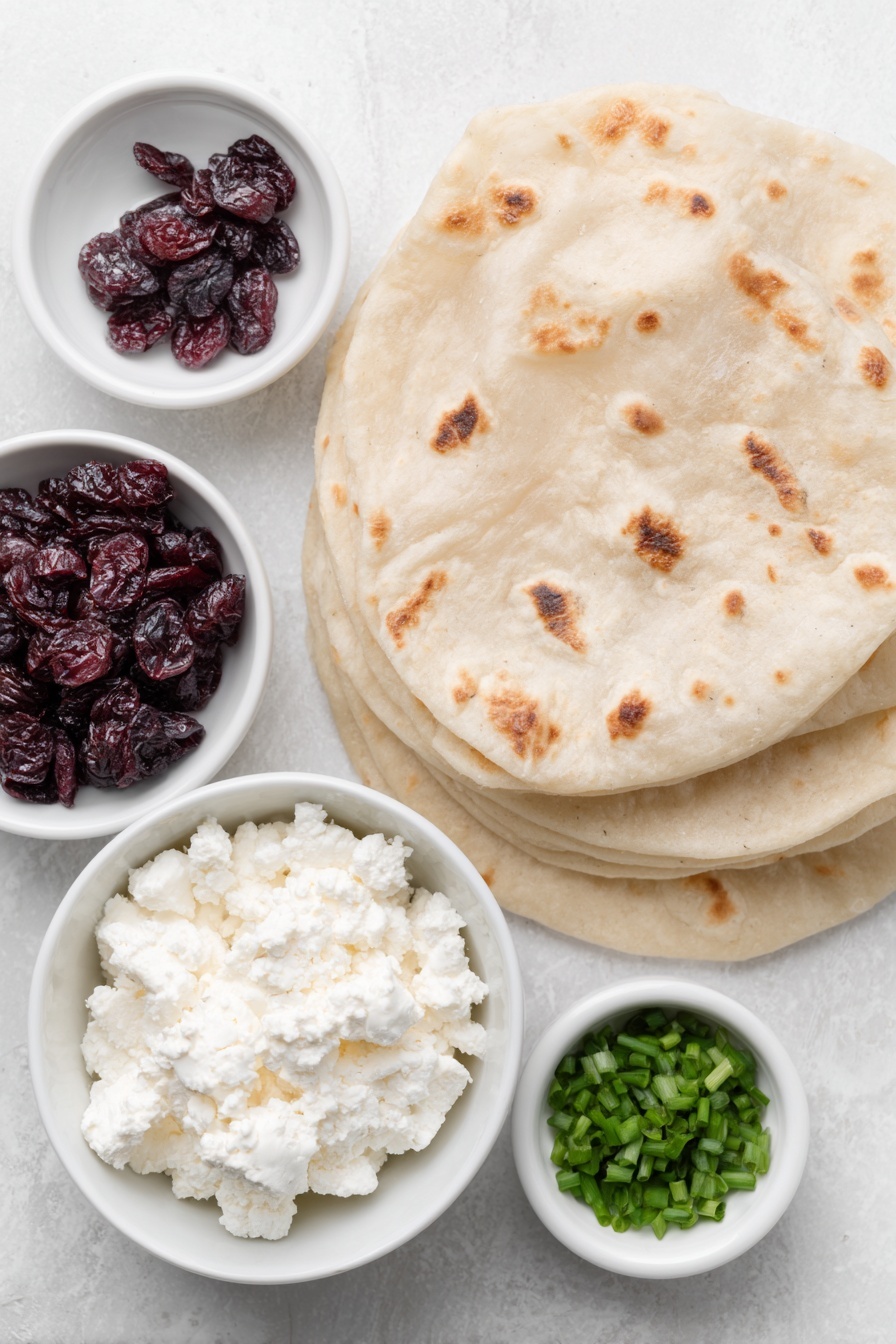 Cranberry Feta Roll-Ups Recipe 7 Flat lay of crumbled sheep’s milk feta cheese in a small white ceramic bowl, softened cream cheese in a small white ceramic bowl, sweetened dried cranberries scattered naturally, four whole large flour tortillas stacked neatly, chopped fresh chives in a small white ceramic bowl, all arranged with perfect symmetry and balanced proportions placed on a clean white marble surface, soft natural light, photo taken with an iPhone, professional food photography style, fresh ingredients, white ceramic bowls, no bottles, no duplicates, no utensils, no packaging --ar 2:3 --v 7 --p m7354615311229779997 - Cranberry Feta Roll-Ups, cranberry feta appetizer, holiday snack ideas, festive party appetizers, easy cheese and cranberry bites