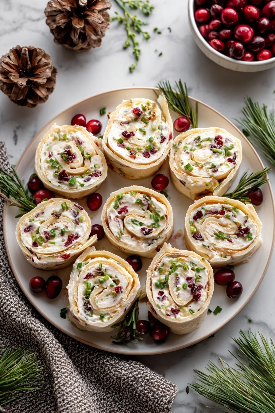 Cranberry Feta Roll-Ups Recipe 6 The dish shows eight rolled pinwheel slices on a round white plate, each slice revealing multiple layers of light beige wrap and creamy white filling mixed with small red cranberry bits and green chive pieces on top. The pinwheels are arranged in a circular pattern with extra whole red cranberries and green pine sprigs placed around them for decoration. The plate sits on a white marbled surface with pinecones, a textured gray cloth, and a small white bowl of cranberries nearby enhancing the festive setting. Photo taken with an iphone --ar 2:3 --v 7 - Cranberry Feta Roll-Ups, cranberry feta appetizer, holiday snack ideas, festive party appetizers, easy cheese and cranberry bites