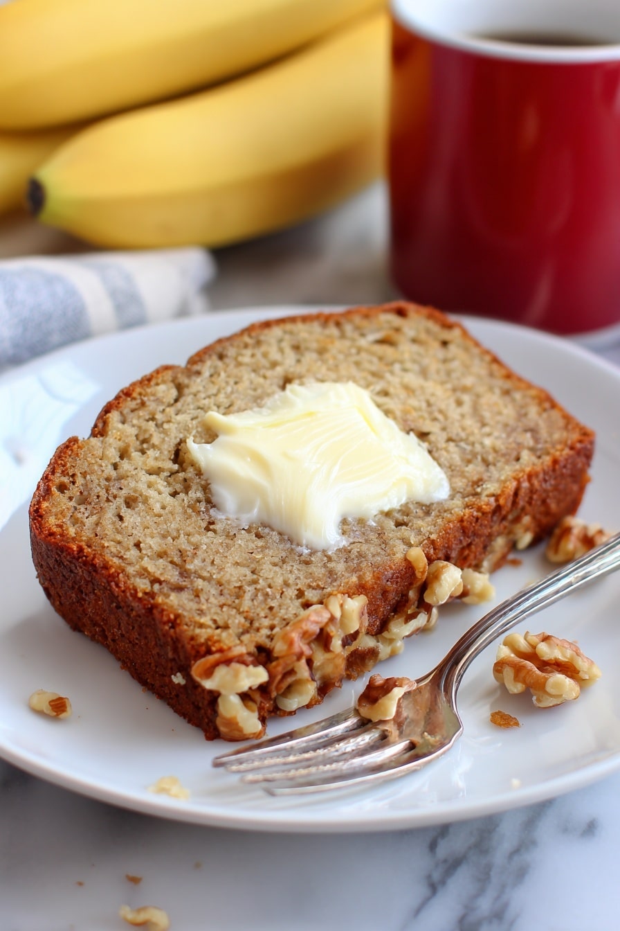 Perfect Banana Nut Bread Recipe 8 The image shows four slices of banana bread stacked slightly overlapped on a wooden board with a white marbled texture beneath. Each slice has a golden-brown crust and a soft light brown inside with visible bits of banana and small walnut pieces. The top slice has a spread of melting white butter in the middle, creating a creamy texture. Scattered around the bread are whole walnut halves, and two ripe spotted bananas rest on the side. In the bottom right corner, a shiny metal butter knife with some butter on its blade lies on the board. The whole scene has warm, natural lighting, giving a cozy feel. photo taken with an iphone --ar 2:3 --v 7 - Perfect Banana Nut Bread, banana nut bread recipe, moist banana bread, easy banana bread, homemade banana bread