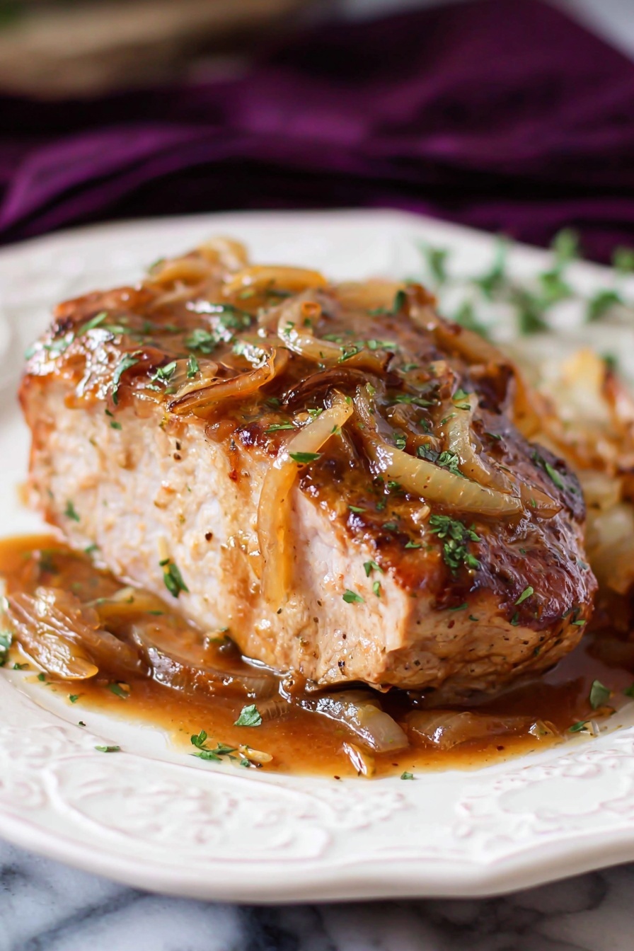 French Onion Pork Chops Recipe 6 A thick piece of cooked meat sits on a white decorative plate with a small side piece next to it. The meat is light brown inside and covered with a shiny layer of sauce on top and around it, mixed with cooked, golden-brown onion strips and sprinkled with chopped green herbs. The sauce looks rich and glossy with a smooth texture. The plate rests on a white marbled surface with a dark purple cloth blurred in the background. Photo taken with an iphone --ar 2:3 --v 7 - French Onion Pork Chops, pork chop recipes with onions, easy pork chop dinner, caramelized onion pork chop skillet, cheesy pork chop bake