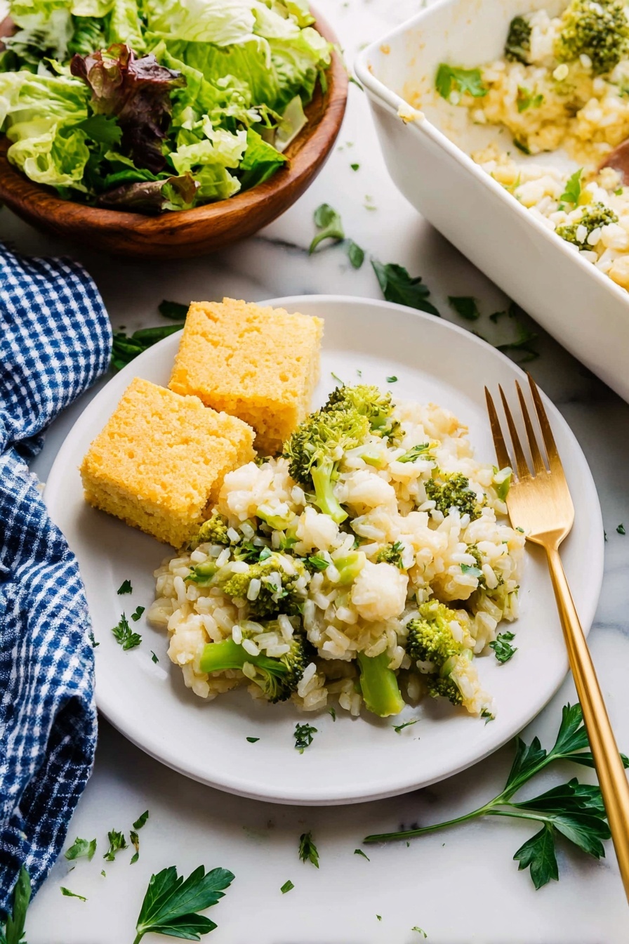Easy Chicken Broccoli Rice Casserole Recipe 8 On a white plate, there is a serving of creamy rice mixed with green broccoli pieces and small white cauliflower chunks, sprinkled lightly with green herbs on top. Two square pieces of golden-yellow cornbread rest beside the rice on the left side of the plate. A gold fork is placed to the right edge of the plate, partially under the rice. The plate is set on a white marbled surface with scattered green parsley leaves around. To the top left, there is a wooden bowl filled with mixed green leafy salad. A blue and white checked cloth lies folded partially under the plate on the left side. At the top right, there is a white dish containing more of the rice and broccoli mixture. photo taken with an iphone --ar 2:3 --v 7 - Easy Chicken Broccoli Rice Casserole, chicken broccoli rice bake, simple chicken and broccoli casserole, quick dinner recipes, hearty rice casserole