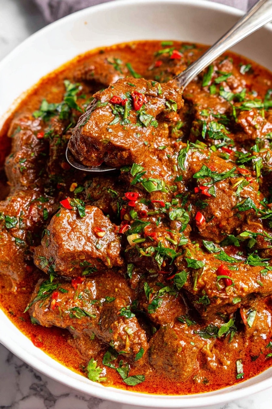 Classic Beef Carne Guisada Recipe 6 A close-up view of a white bowl filled with a thick stew made of brown meat chunks covered in a rich, smooth reddish-brown sauce. The dish is sprinkled generously with bright green chopped herbs and small red chili flakes, adding texture and color contrast on top. A silver spoon holds a few pieces of the meat and sauce above the stew, showing the creamy consistency and tender texture of the meat. The background is a white marbled surface. photo taken with an iphone --ar 2:3 --v 7 - Classic Beef Carne Guisada, beef guisada recipe, hearty beef stew, Mexican beef stew, comfort food recipes