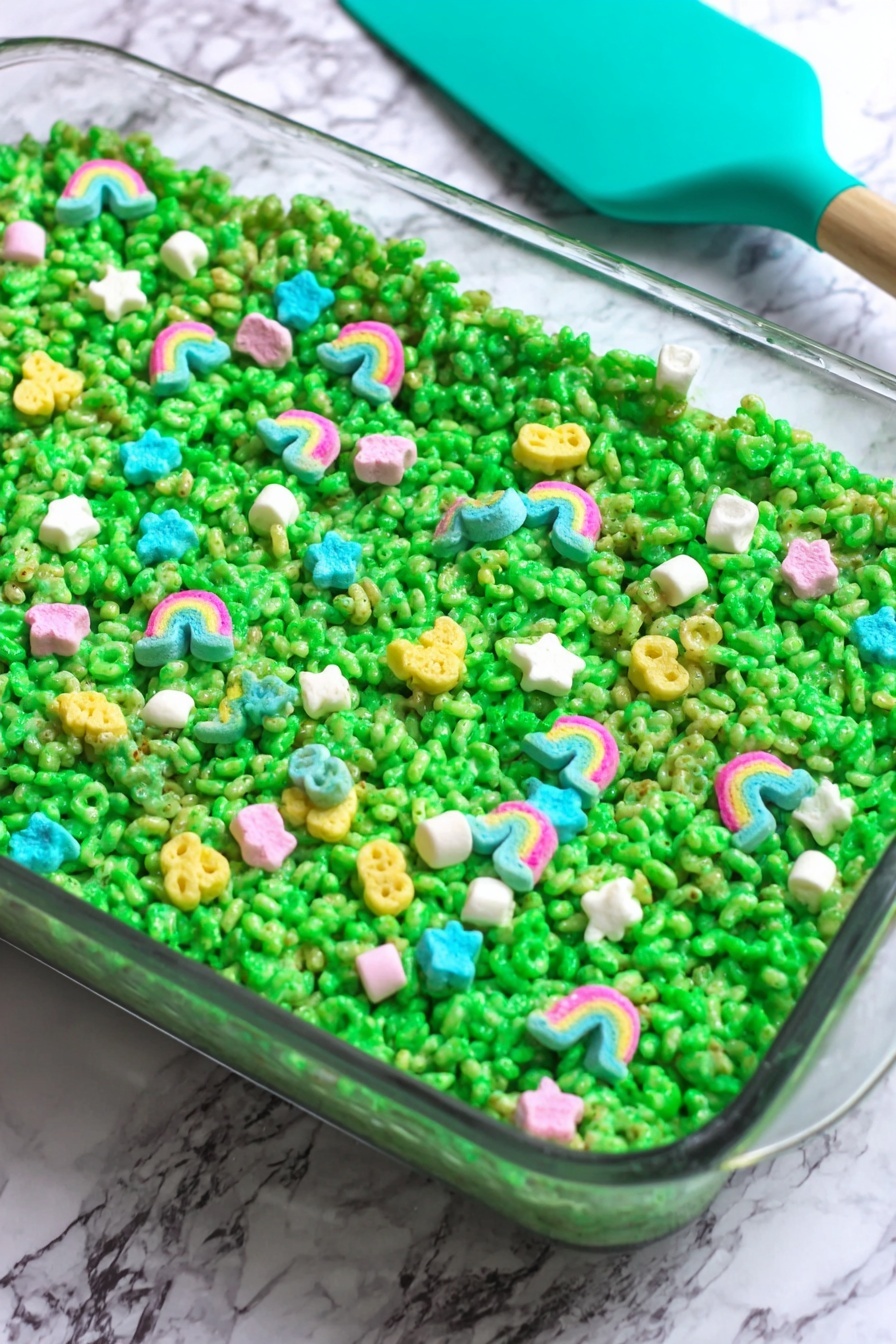 Lucky Charms Rice Krispie Treats Recipe 6 The dish is a single green layer made of puffed cereal tightly packed in a clear glass rectangular dish, with the bright green layer showing a slightly sticky and shiny texture. Scattered evenly on top are colorful, small marshmallow shapes including rainbows, stars, and other shapes in pastel colors like pink, blue, yellow, and white, adding pops of color against the green. The background is a white marbled surface with a teal silicone spatula resting on the upper left edge of the dish. photo taken with an iphone --ar 2:3 --v 7 - Lucky Charms Rice Krispie Treats, colorful cereal treats, marshmallow rice krispie bars, fun kid-friendly desserts, quick no-bake treats