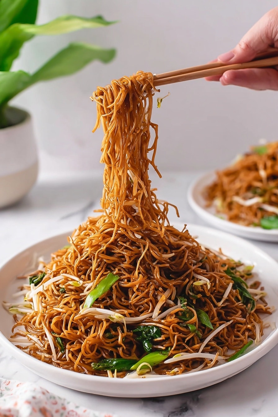 Cantonese Chow Mein Stir Fry Recipe 8 A white bowl filled with a large serving of thin brown noodles mixed with white bean sprouts and green leafy vegetables. Above the bowl, a woman's hand is holding light-colored chopsticks lifting a thick bundle of noodles and some greens, showing their long and curly texture. In the background, there is another white bowl with more noodles and a small green plant in a white pot. The setting rests on a white marbled surface with a pink and white checkered cloth placed in the foreground. Photo taken with an iphone --ar 2:3 --v 7 - Cantonese Chow Mein Stir Fry, Chinese noodle stir-fry recipe, crispy chow mein noodles, easy Cantonese stir-fry, takeout-style noodle dish