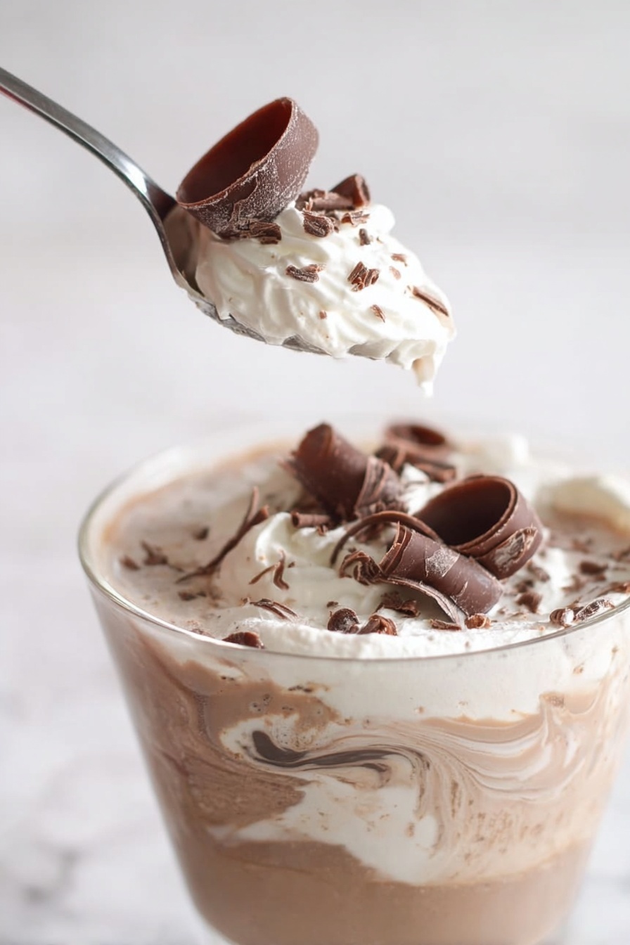Chocolate Mocha Party Punch Recipe 6 A close-up of a clear glass cup filled with a layered drink featuring swirls of light brown and creamy white, topped with a generous layer of whipped cream. On top of the cream are delicate chocolate curls in dark brown scattered around. A spoon is lifted above the cup with a swirl of whipped cream and a single large chocolate curl resting on it. The background and surface show a white marbled texture. The lighting is soft, highlighting the smooth texture and gentle swirl of the drink, making it look rich and creamy. photo taken with an iphone --ar 2:3 --v 7 - Chocolate Mocha Party Punch, chocolate mocha punch recipe, coffee chocolate party drink, creamy mocha punch, festive chocolate coffee punch