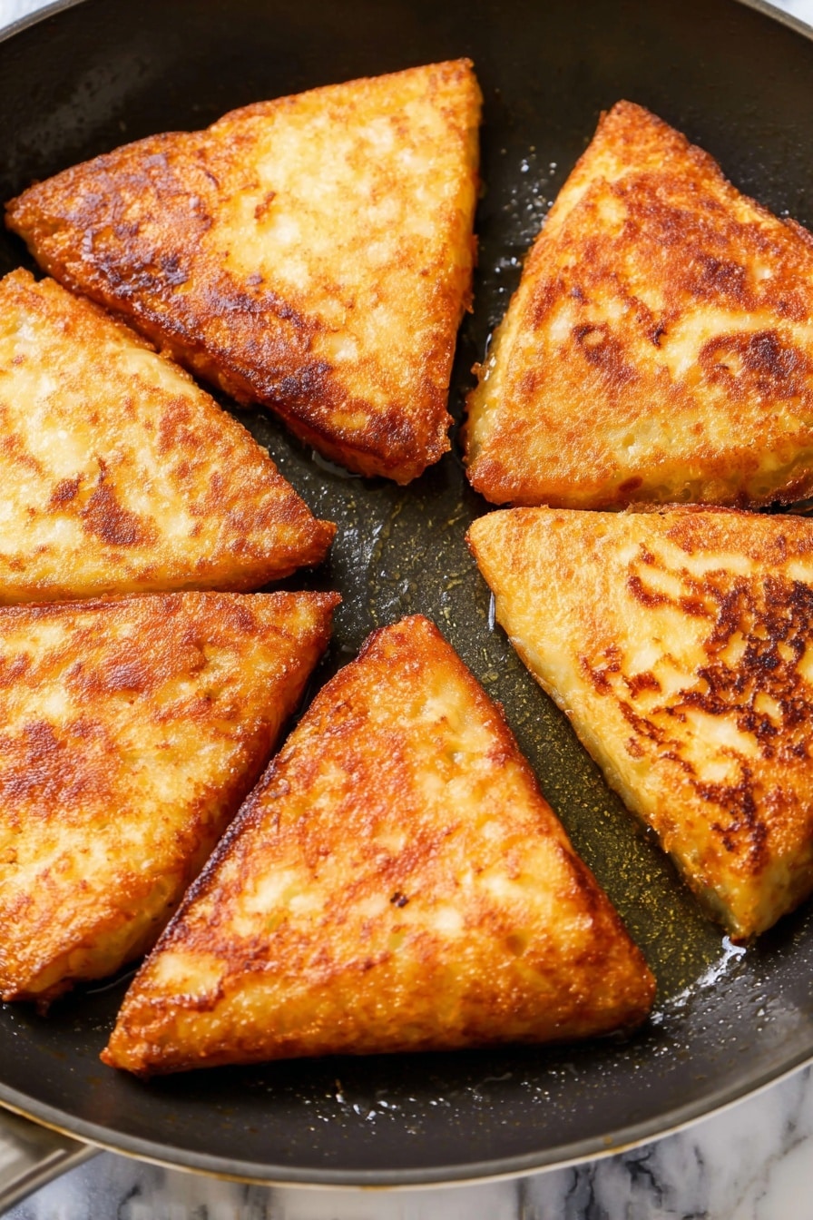 Irish Potato Farls Recipe 6 The image shows five triangular pieces of fried golden brown food arranged inside a black frying pan. Each triangle has a crispy, slightly uneven surface with areas of darker brown spots, indicating a crunchy texture. The pieces are sitting close to each other with visible oil around them inside the pan. The background below the pan is changed to a white marbled texture. photo taken with an iphone --ar 2:3 --v 7 - Irish Potato Farls, Irish Potato Farls recipe, Irish potato bread, traditional Irish farls, easy Irish bread